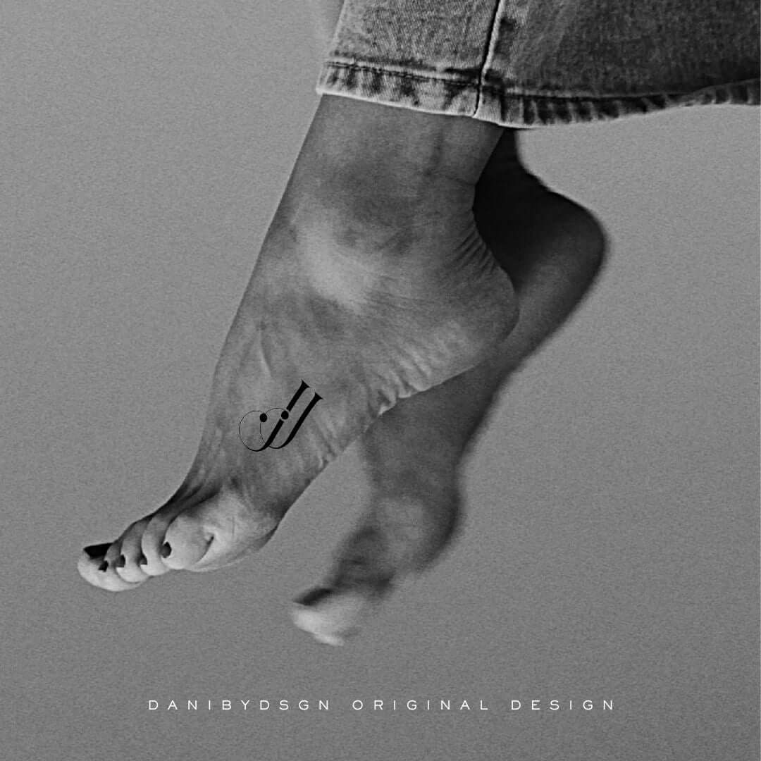 A monochrome image highlighting a 'jj' two initial monogram tattoo design on the inner ankle, created by Danibydsgn. This custom logo design merges the personal branding and tattoos art, creating a unique body art piece. The elegant monogram serves as a testament to the versatile business logo designs suitable for personal branding, clothing branding, and special event marketing. Danibydsgn's work as a graphic designer is evident, reflecting high-standard branding.
