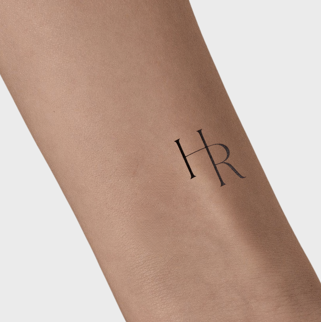 Tattoo of initials 'HR' on a person's arm with a light background
