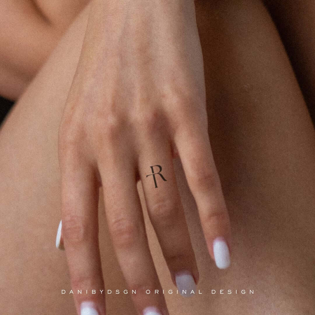 Close-up of a delicate 'TR' Custom Initial Monograms tattoo on a hand, exemplifying Danibydsgn's custom logo design tailored for personal branding, body art and tattoo design. This minimalist name monogram serves as a subtle expression of identity, blending and personal branding. The artful domains of tattoo design, business logo designs, and personal branding. Danibydsgn initial monograms are perfect for wedding monograms, wall art, clothing branding and special event marketing.