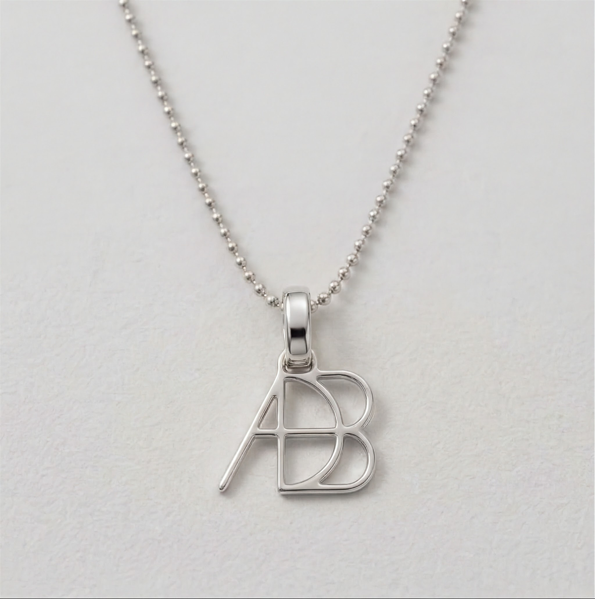 A 925 sterling silver ball chain necklace and custom Danibydsgn design clip-on charm photographed on a light textured surface. Meaningful personalised jewelry from Danibydsgn.