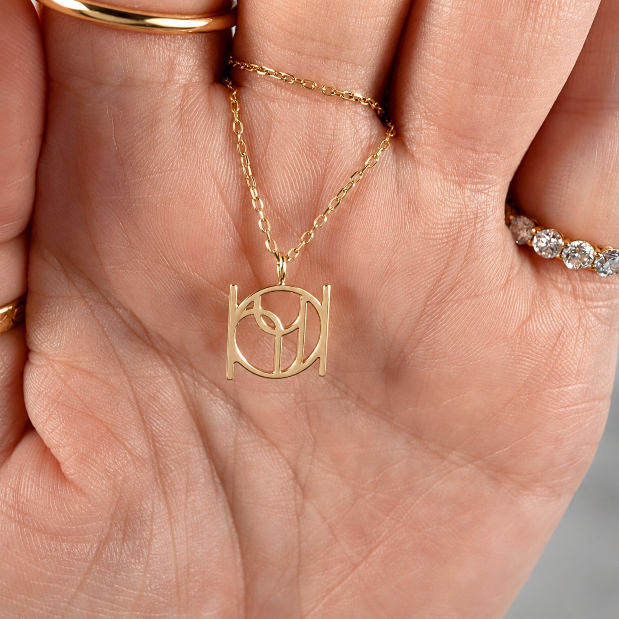 Close-up detail of a custom symbol pendant necklace in solid 9k gold resting in a hand, showing the fine cut-out Danibydsgn design and the central jump ring connection.
