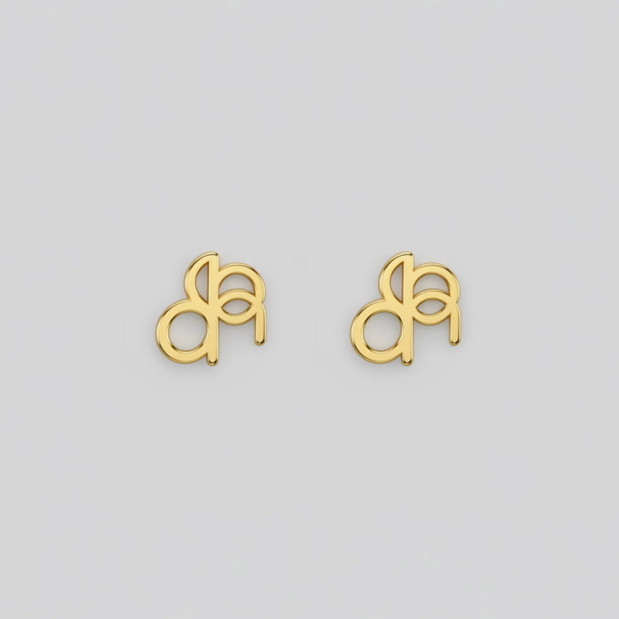 A pair of Danibydsgn custom symbol earings in a lowercase design in 9k gold on a white back ground.