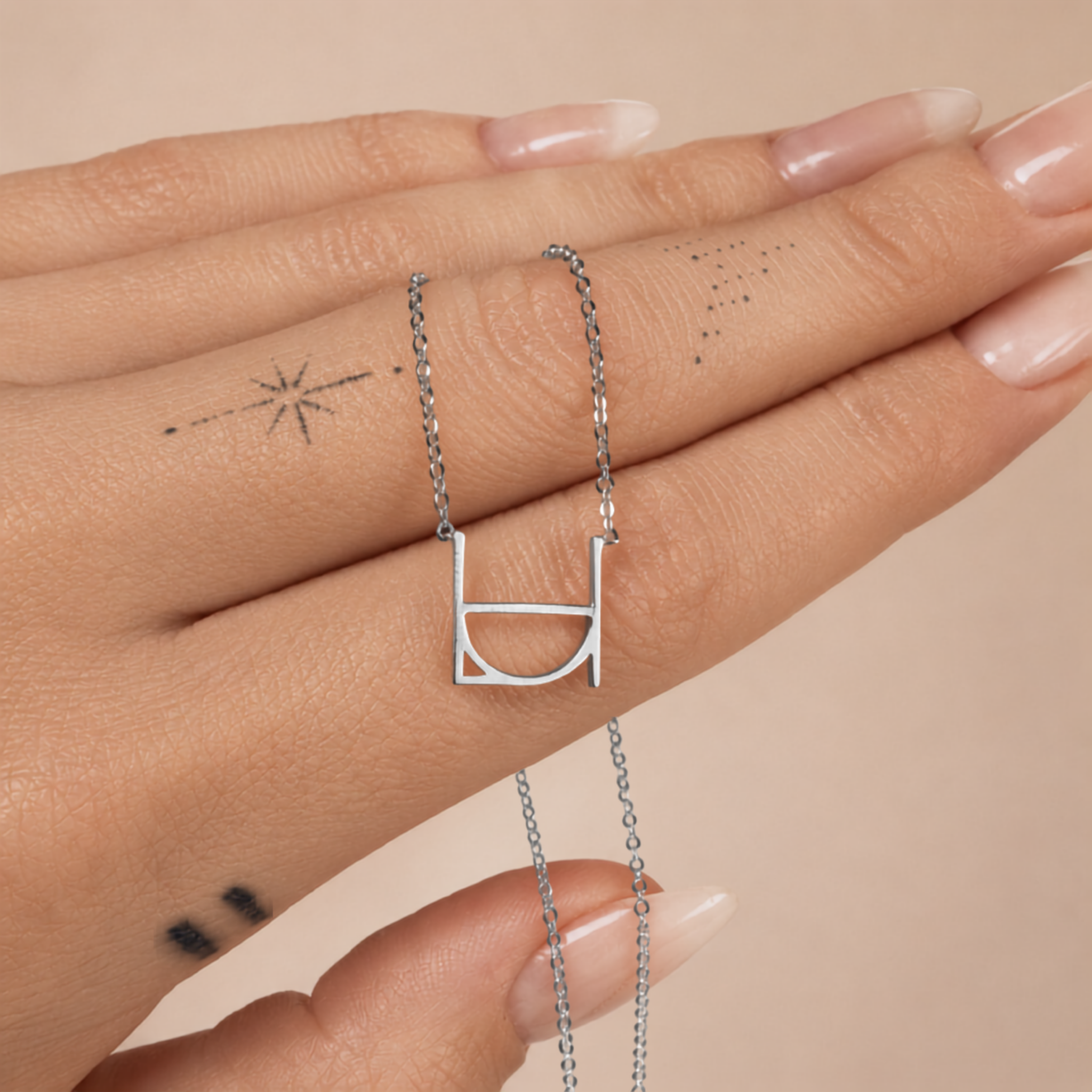 A close-up product shot of a model's hand laid horizontally, displaying the Danibydsgn single symbol pendant necklace in 925 sterling silver. The delicate silver chain is draped over a finger to show the precise scale and fine architectural silhouette of the personalized geometric initial charm against a neutral background.