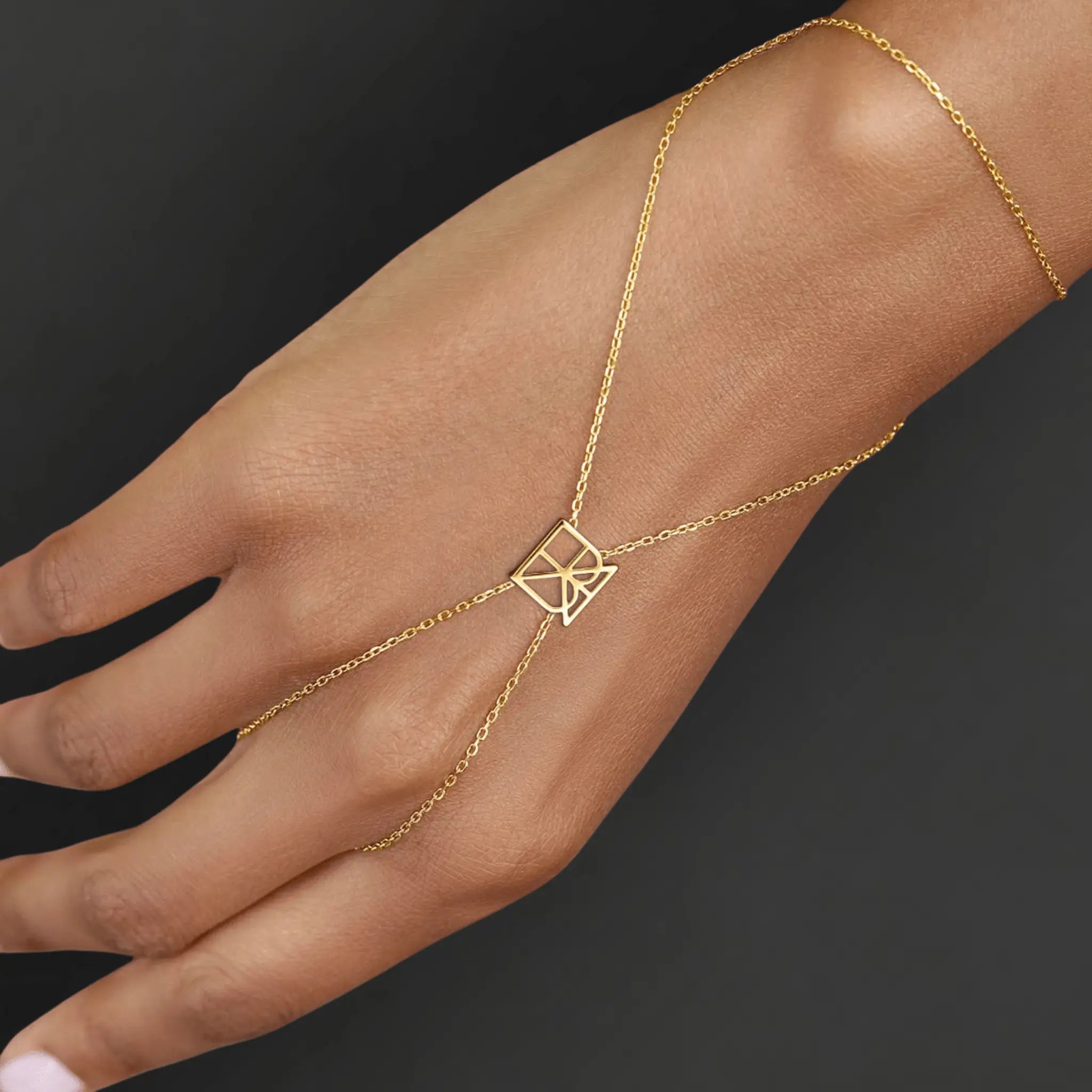 Danibydsgn custom symbol hand chain in 9K gold worn on hand, showing the fine chain drape and geometric cut-out symbol connector.
