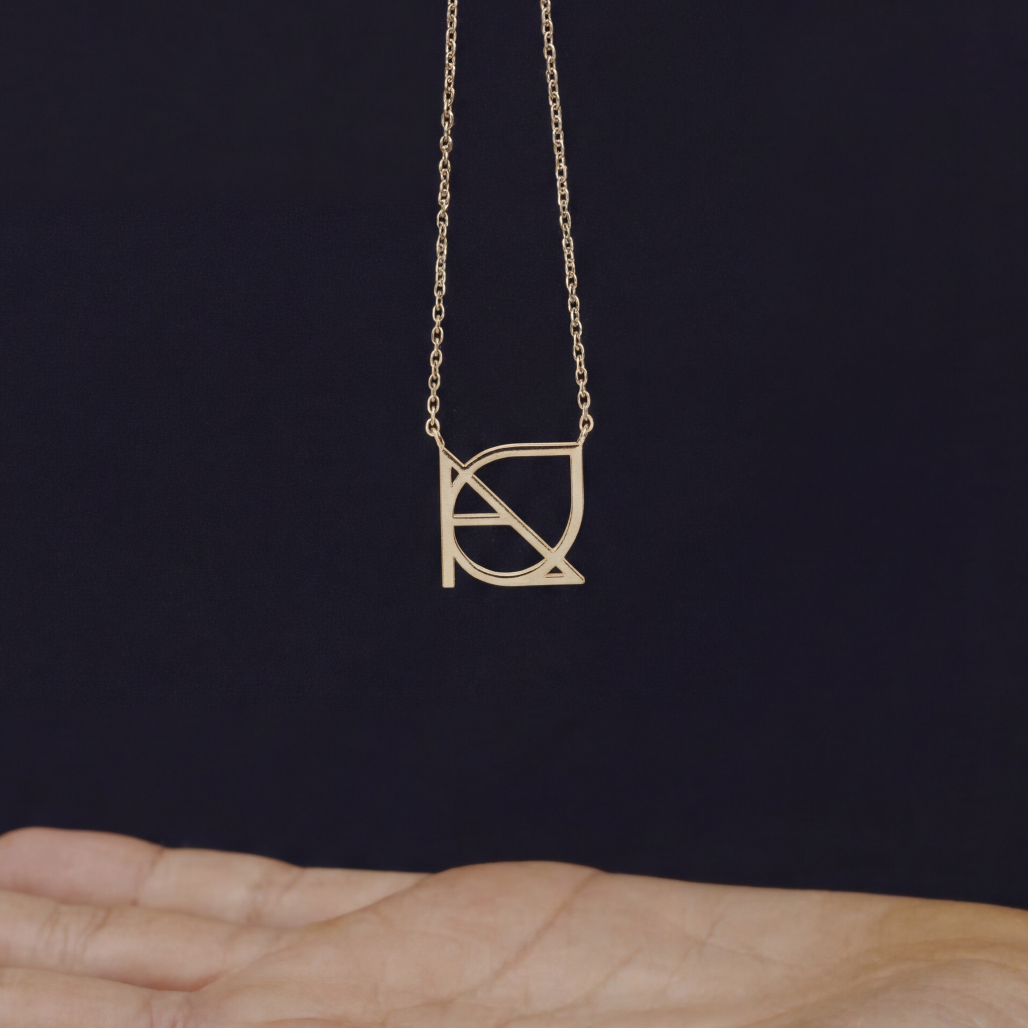 A custom necklace in 9k gold suspended above an open palm, showcasing a piece of meaningful jewelry with a unique hand-designed Danibydsgn symbol cut out jewelry pendant featuring a side-welded chain layout.