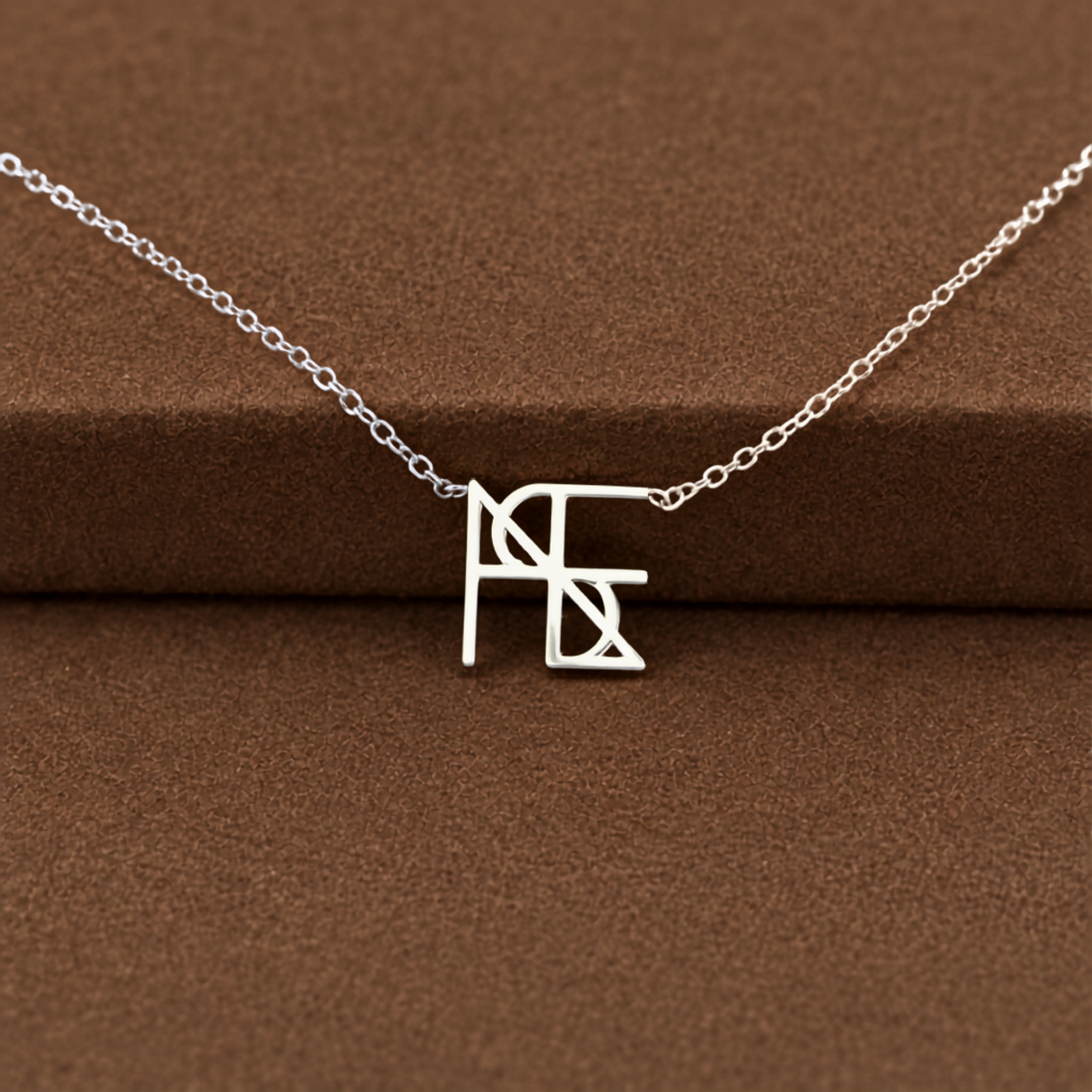 A close-up studio product shot of the Danibydsgn single symbol pendant necklace in 925 sterling silver. This dainty silver necklace features one personalized uppercase geometric initial charm handcrafted from a custom line art design, resting elegantly across a textured brown velvet jewelry display surface.