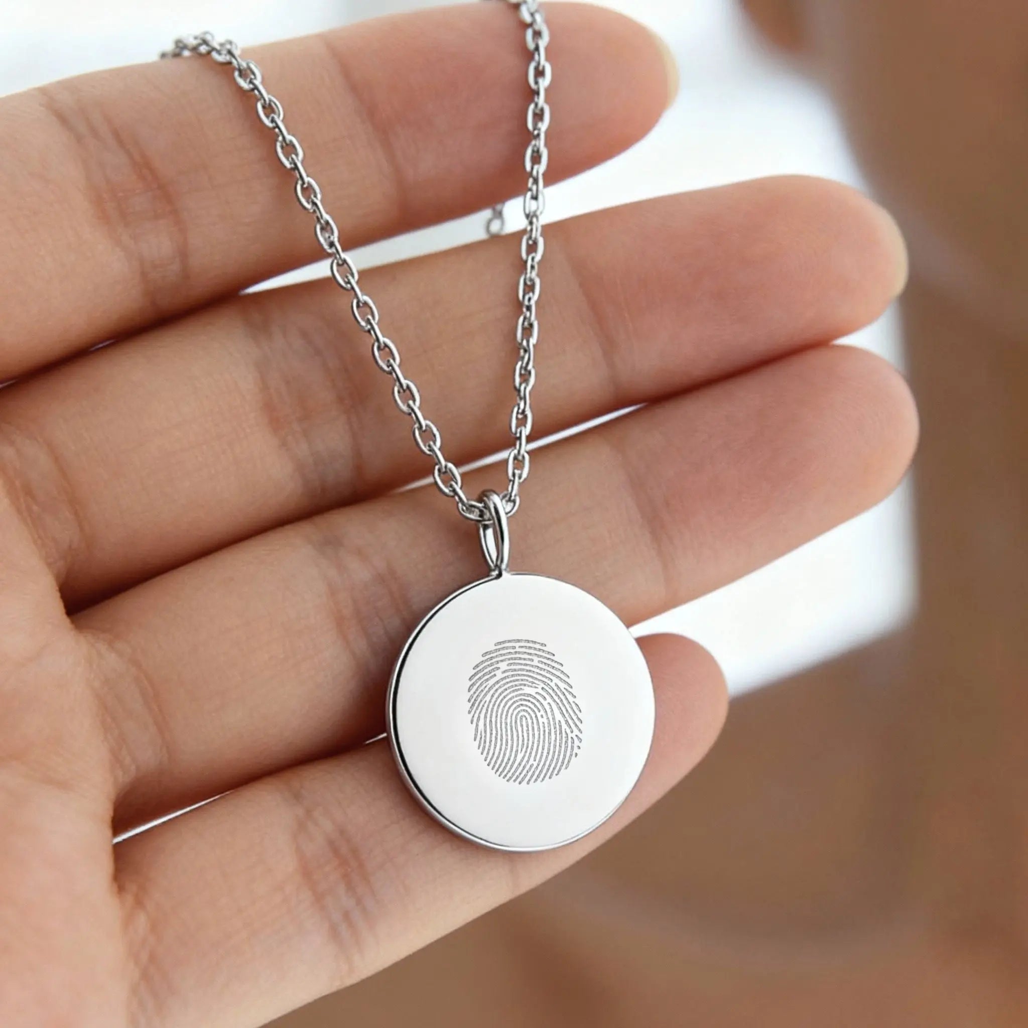 Sterling silver single fingerprint coin necklace by Danibydsgn held in a hand, showcasing its elegant design.