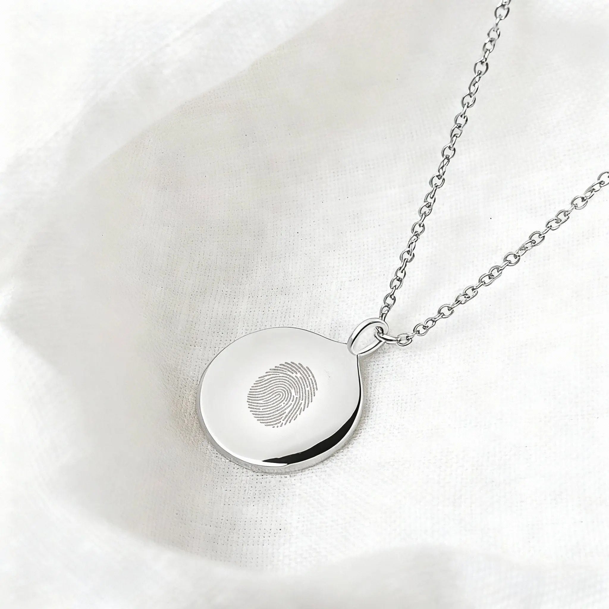 Luxury 925 sterling silver single fingerprint coin necklace by Danibydsgn on a soft fabric background.
