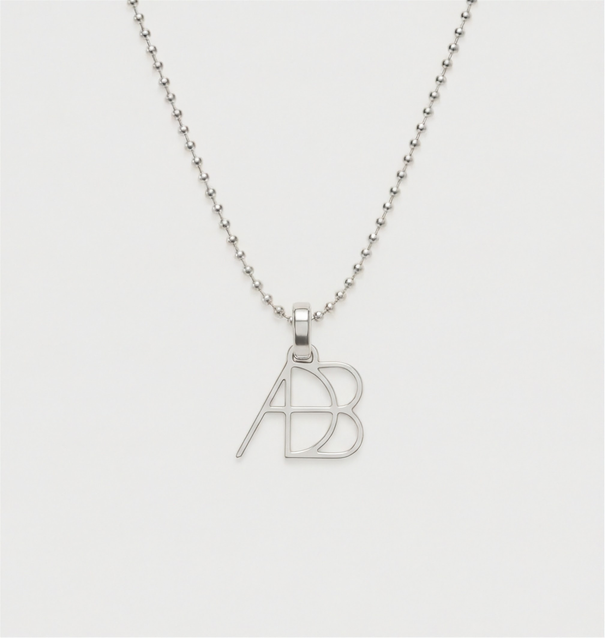 A close up shot of a 925 sterling silver ball chain necklace and custom Danibydsgn symbol design clip-on charm photographed on a light back ground. Meaningful personalised jewelry from Danibydsgn.