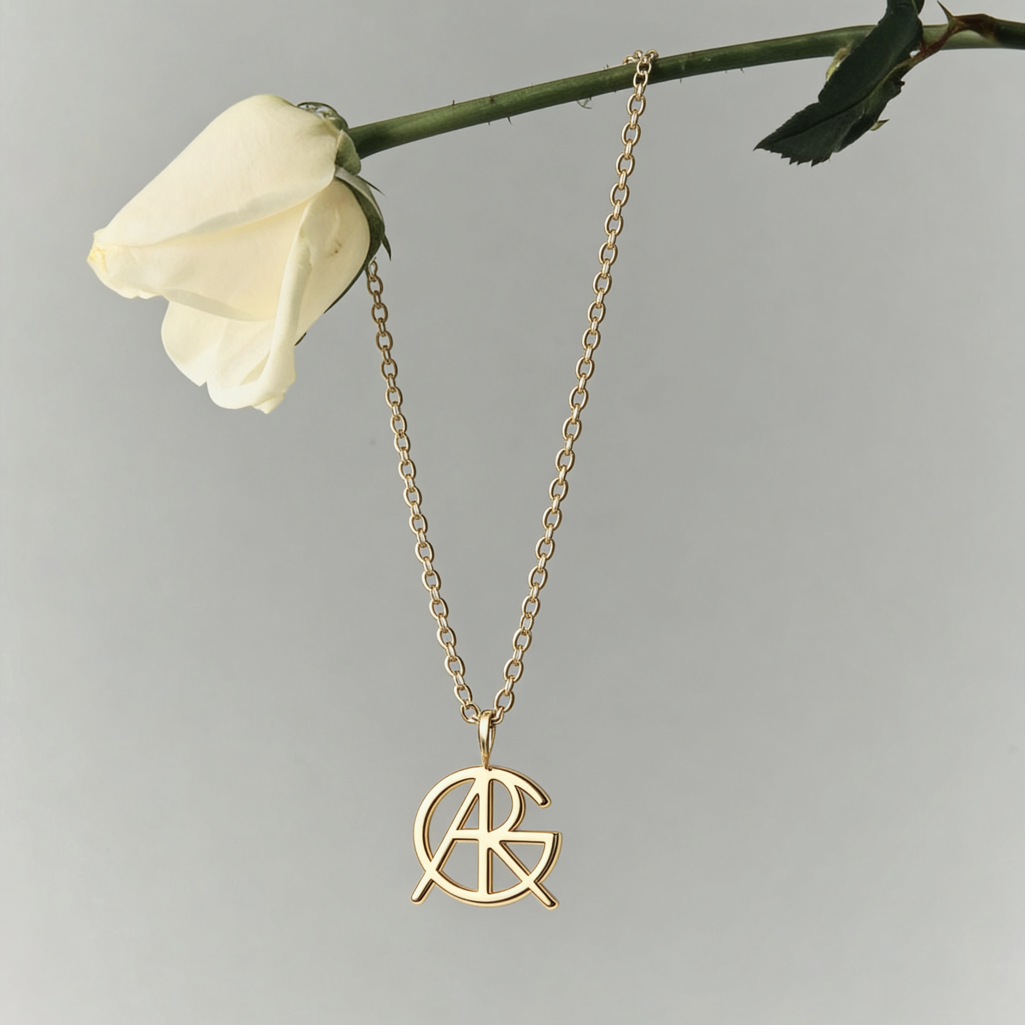 A 9k gold custom necklace hanging from a white rose stem, showcasing a piece of minimalist jewelry featuring a meaningful jewelry Danibydsgn symbol cut out jewelry pendant with a top jump ring.