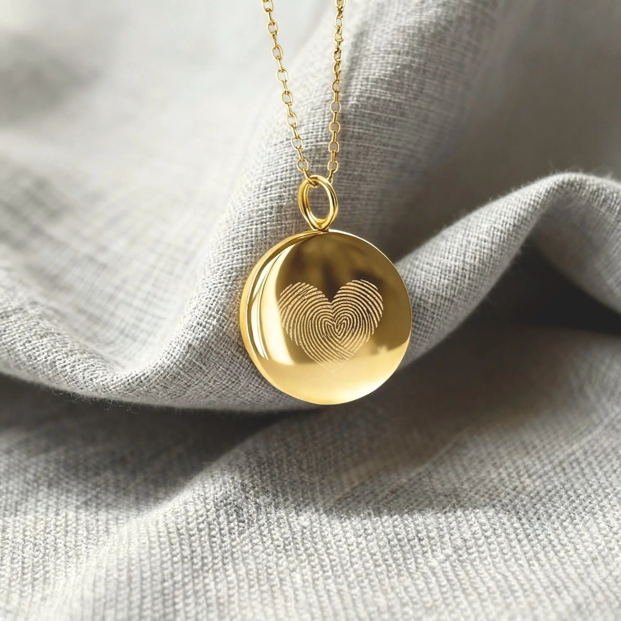 Close-up of the Heart Fingerprint Coin Pendant Necklace in 18K Gold Vermeil by Danibydsgn resting on soft fabric. The pendant features two fingerprints engraved in a heart shape, symbolising eternal love and connection. A luxury personalised necklace crafted with precision and modern elegance.