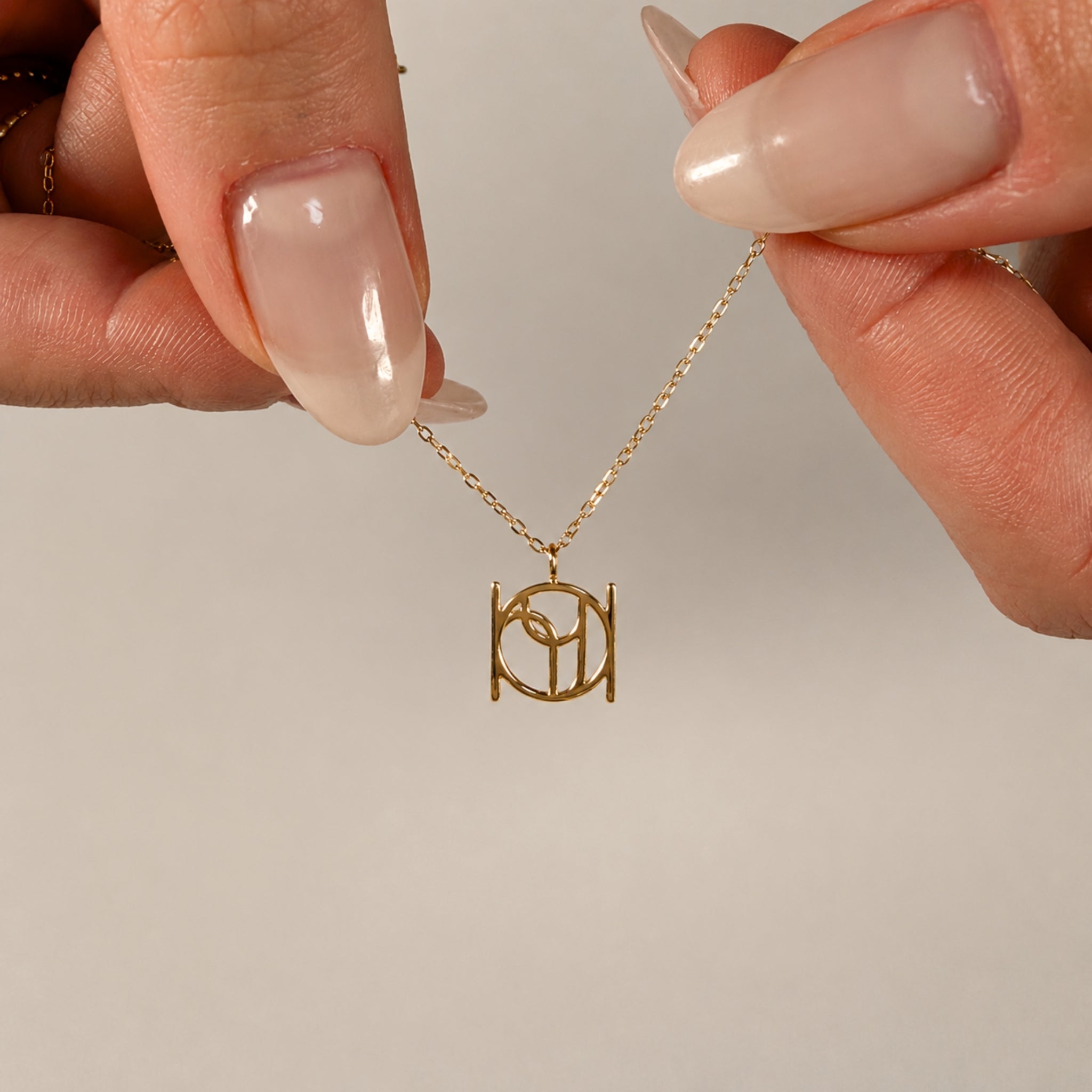 A close-up view of hands holding a fine gold chain to showcase a solid 9k gold Danibydsgn custom single symbol pendant, highlighting the new central single jump ring design that allows the pendant to slide freely.