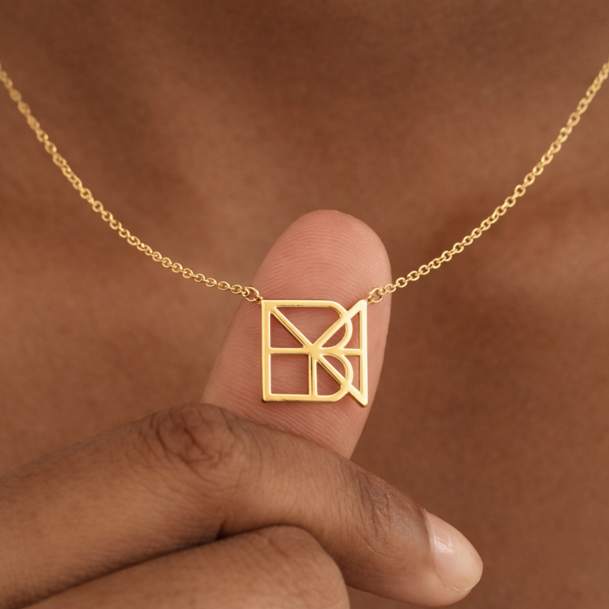 Fingers holding a custom necklace in 9k gold, displaying a meaningful jewelry piece with a unique hand-designed Danibydsgn symbol cut out jewelry pendant featuring a side-welded chain configuration.