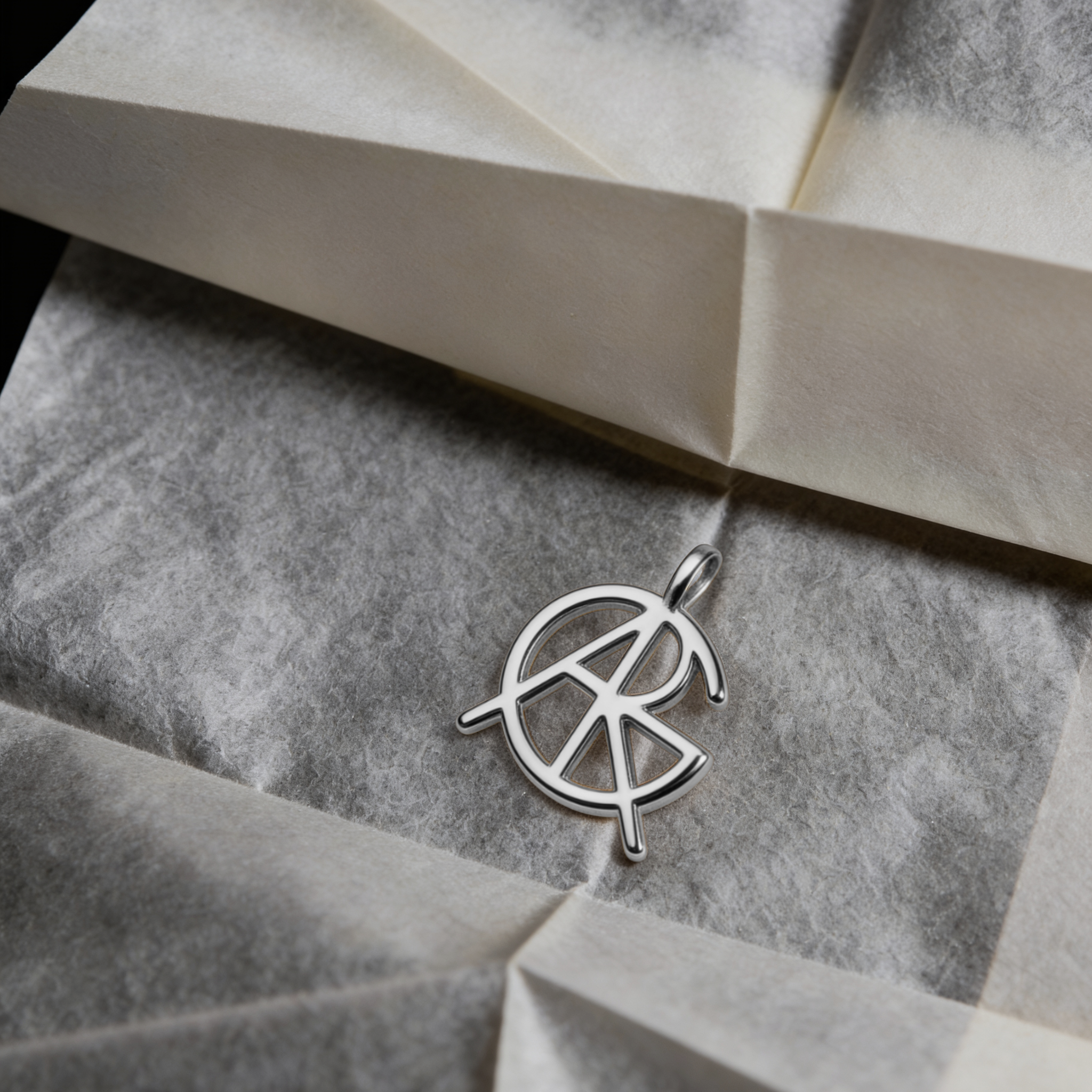 A standalone custom necklace charm option without the chain, showing a meaningful jewelry piece featuring a single hand-designed Danibydsgn symbol cut out jewelry pendant in 925 sterling silver resting on textured paper.