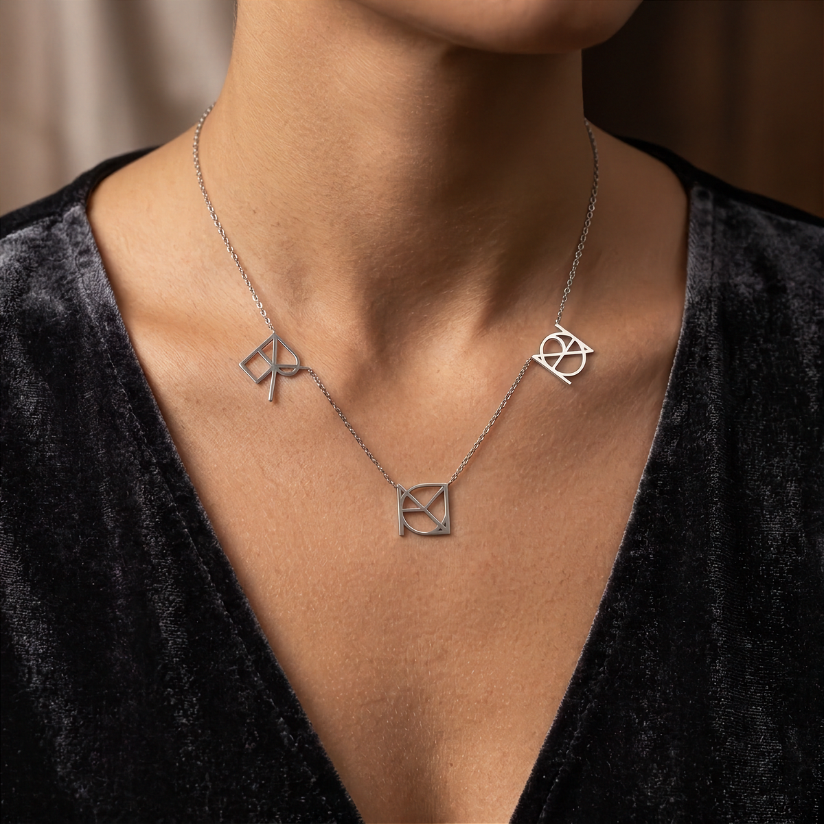 A close-up lifestyle image of an elegant model in a black evening gown wearing the Danibydsgn three symbol pendant necklace in 925 sterling silver. The pic showcases a delicate silver chain with three personalized uppercase geometric charms handcrafted from a custom fine-line Danibydsgn design.