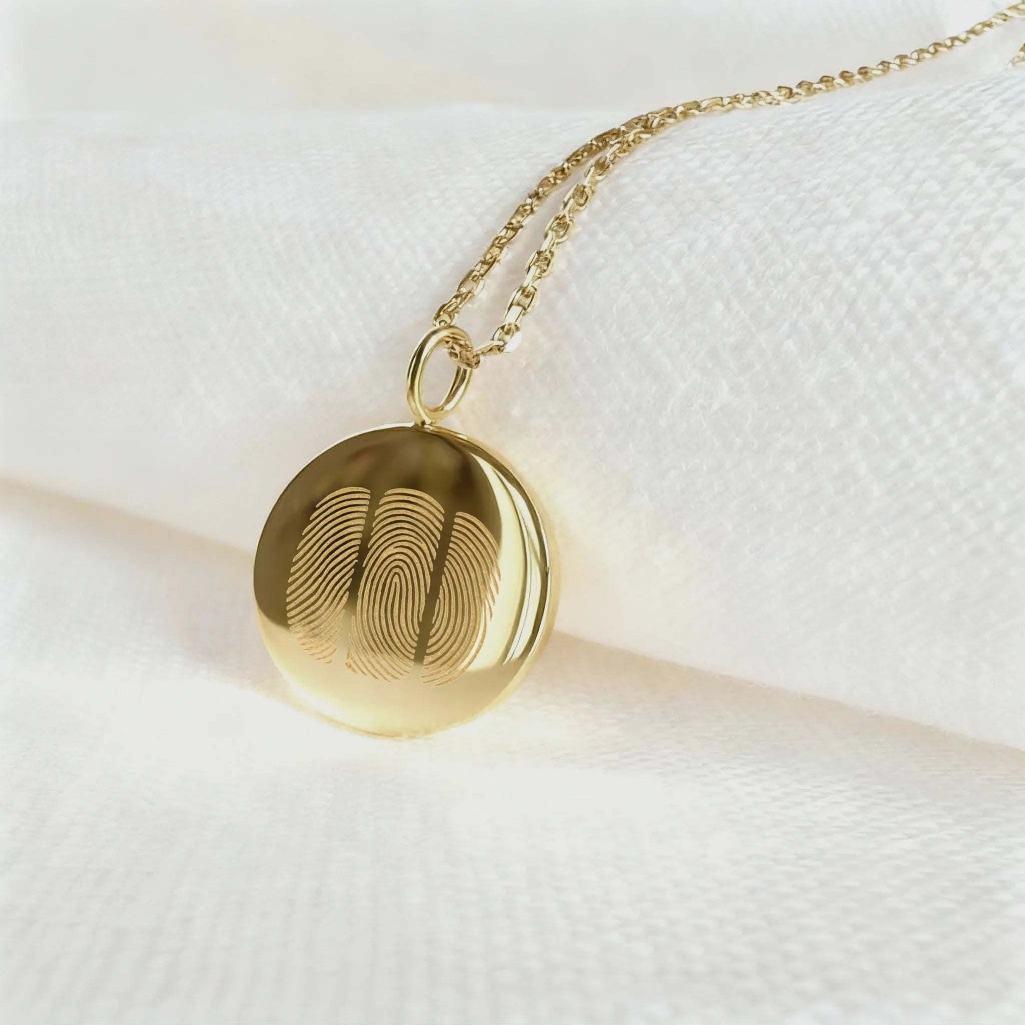 The Luxury Three Fingerprint Coin Necklace in 18K Gold Vermeil by Danibydsgn rests elegantly on a white fabric background. Featuring three detailed fingerprints engraved into a polished gold pendant, this handcrafted piece symbolizes love, memory, and connection in timeless luxury jewelry design.