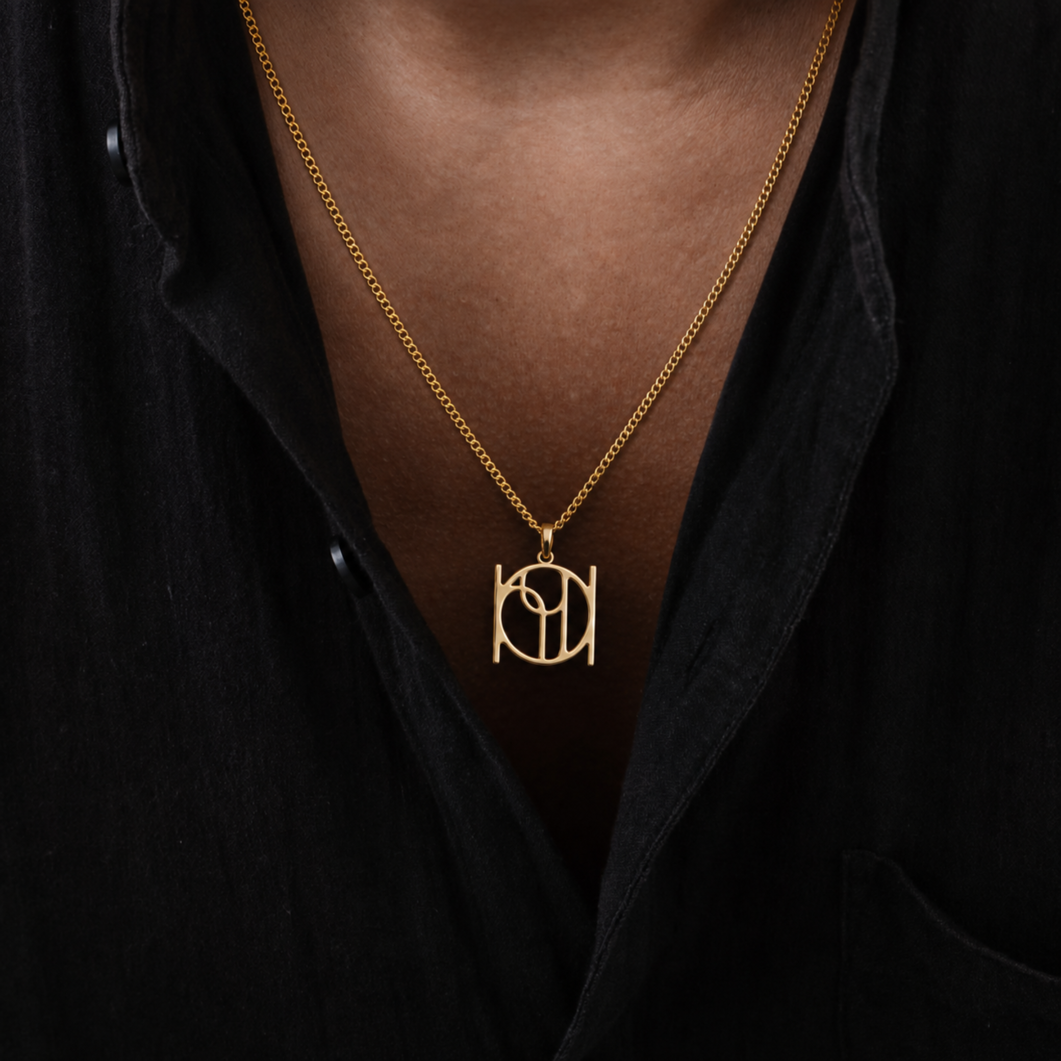 A 9k gold cable chain necklace with a Danibydsgn design symbol pendant worn by a model in a black shirt. Custom jewelry