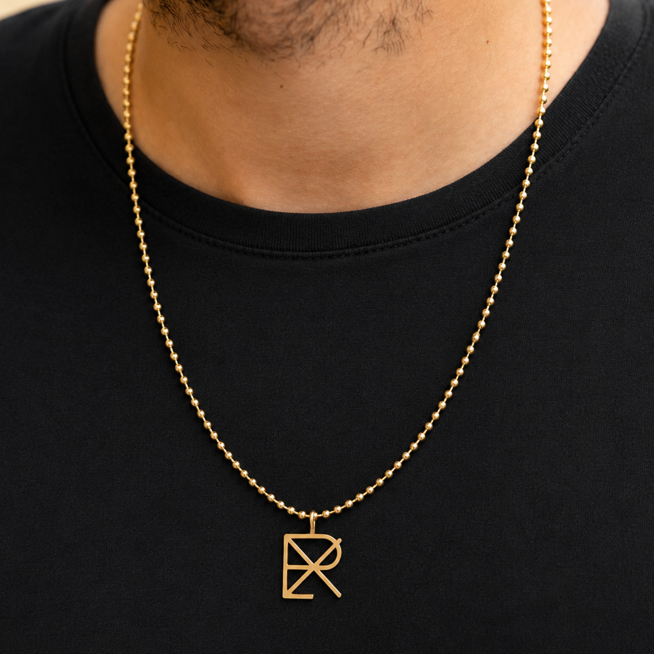 A 9k gold ball chain necklace 20-22inch adjustable chain with a Danibydsgn design cut out symbol pendant, worn by a man wearing a black t-shirt. Meaningful jewelry for him.