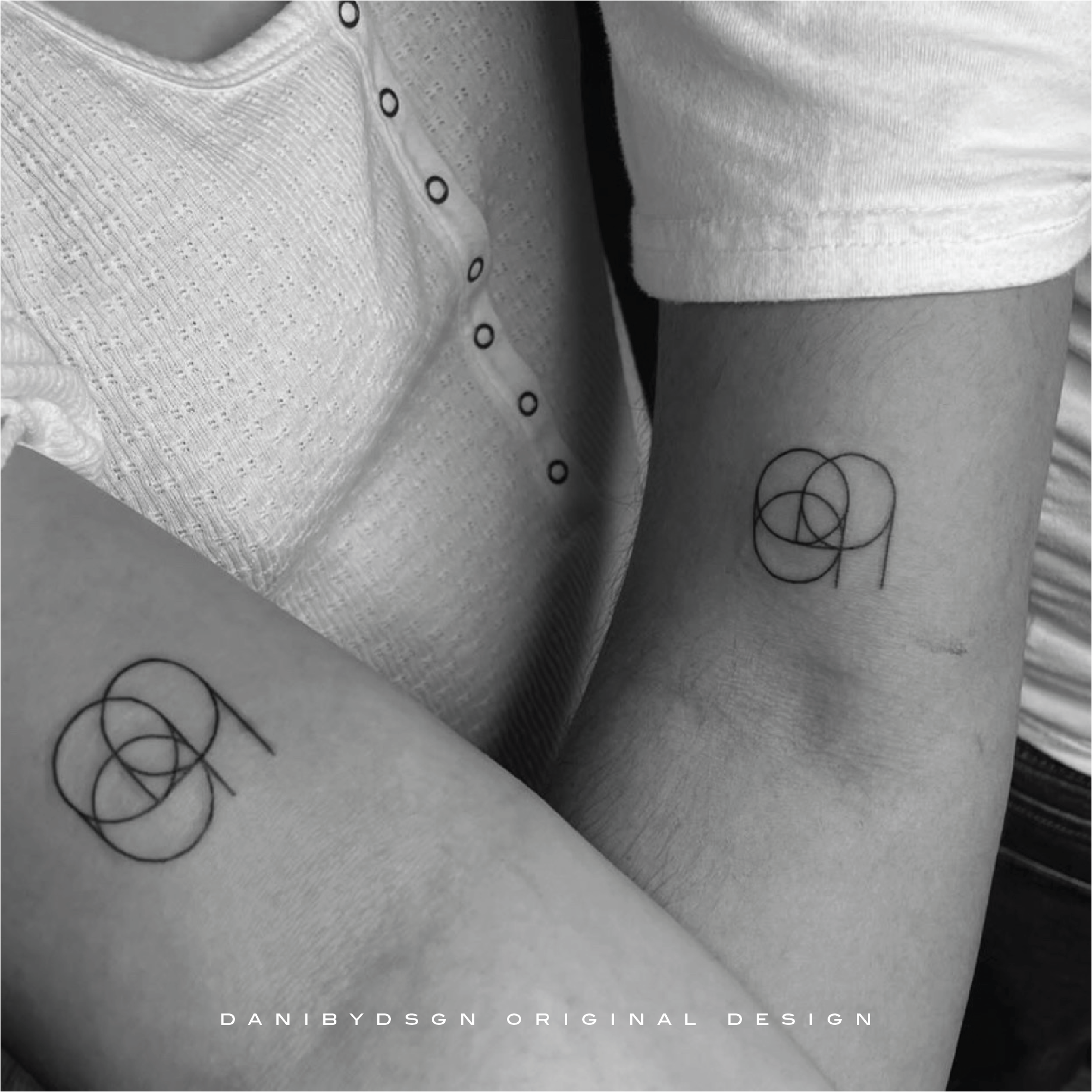 A black and white photograph captures a couple's arms each adorned with a matching single-symbol fineline tattoo representing their wedding date, created by Danibydsgn the original name logo designer. These tattoos are a unique expression of their shared journey, reflecting the duo's personal story through Danibydsgn’s custom design work. Danibydsgn has a reputation for excellence in personal branding and graphic design and has become the go to person for unique, elegant, meaningful logo designs.