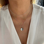 Model wearing the Danibydsgn custom engraved coin necklace in 925 sterling silver, captured in natural light. The reflective pendant rests above a white blouse, paired with a delicate secondary chain for a minimal, layered jewelry look.