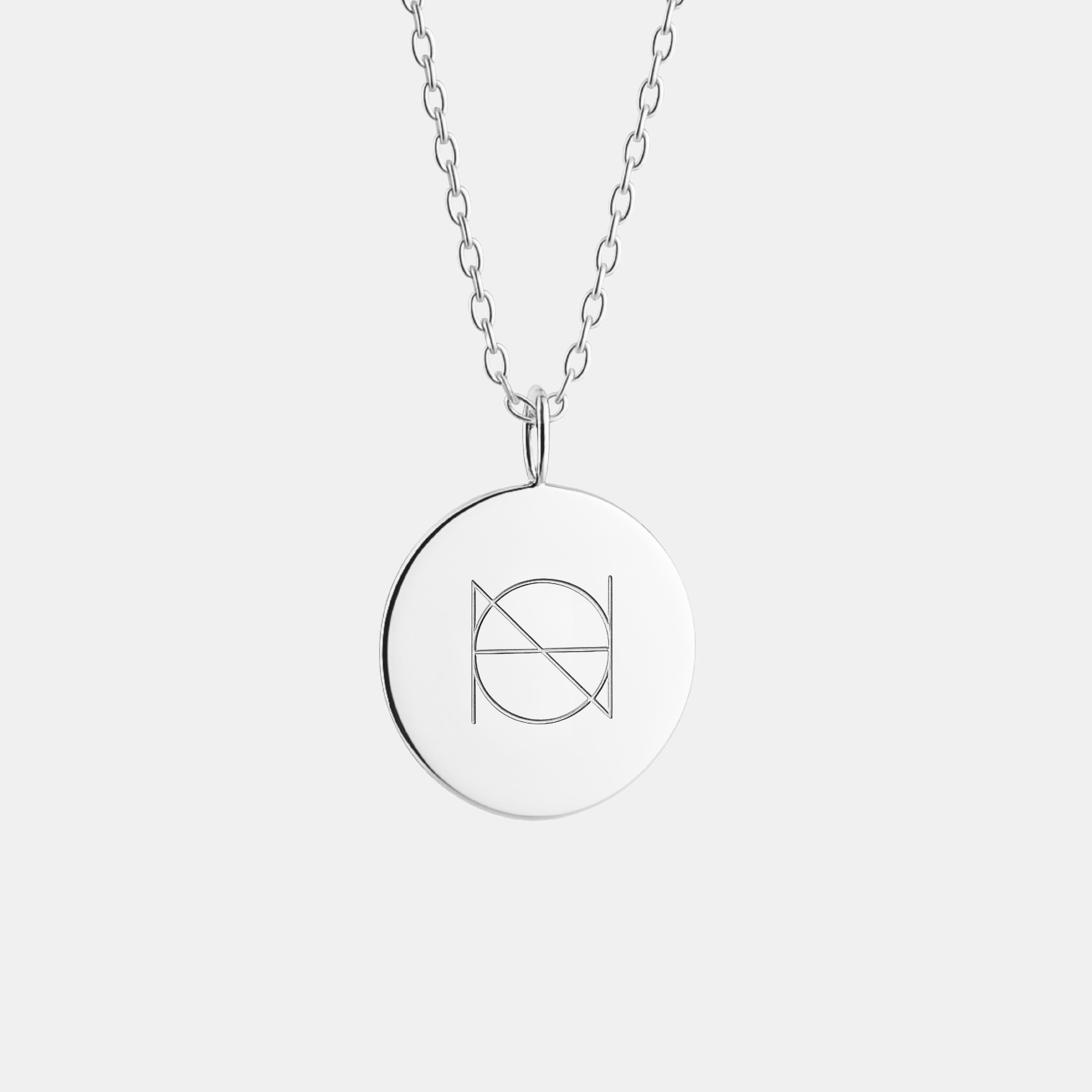 A 925 Sterling Silver coin necklace with an engraved custom Danibydsgn logo design on it, of one symbol on a light coloured background.