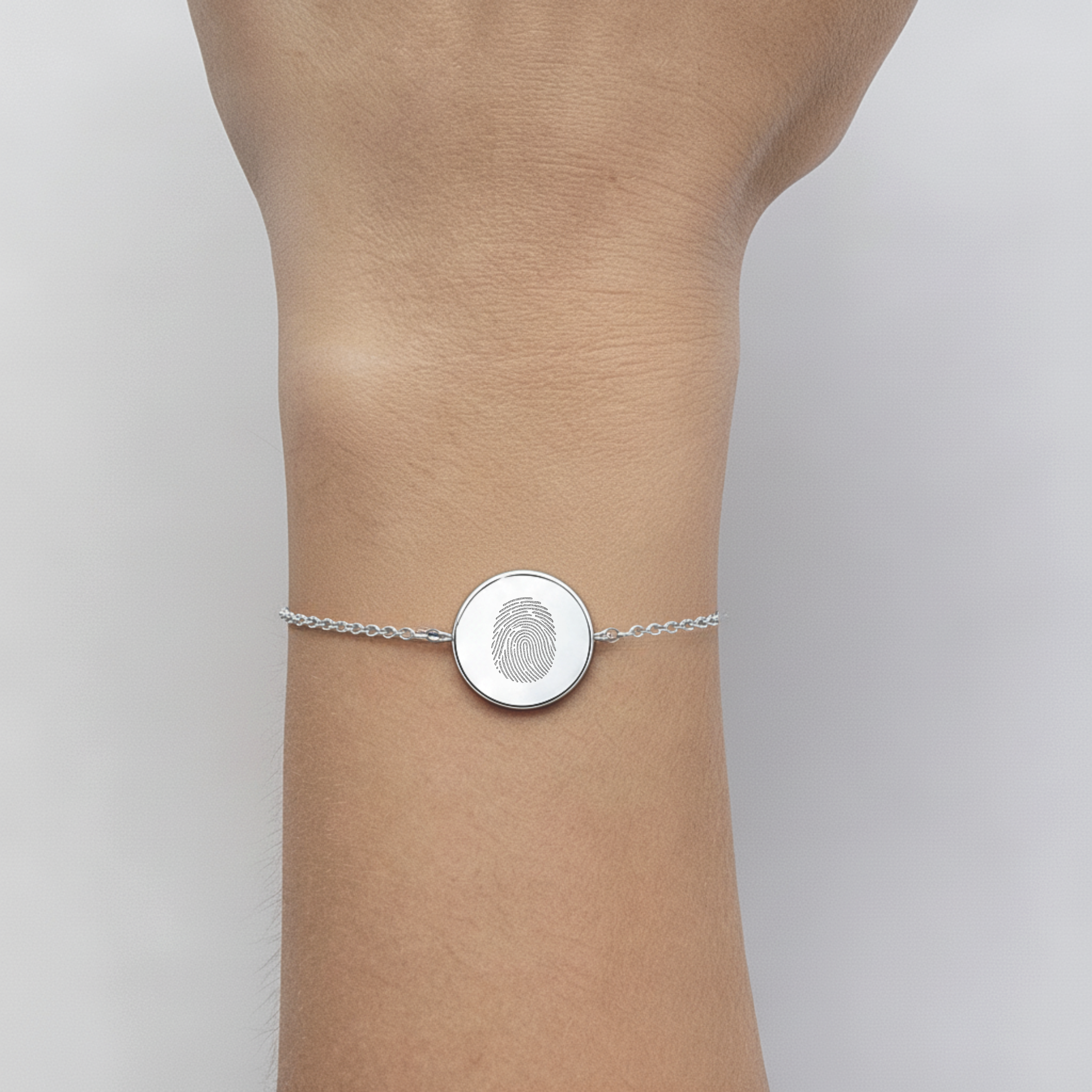 925 Sterling Silver bracelet with a circular coin pendant design engraved with one fingerprints, on a lady's wrist against a neutral background