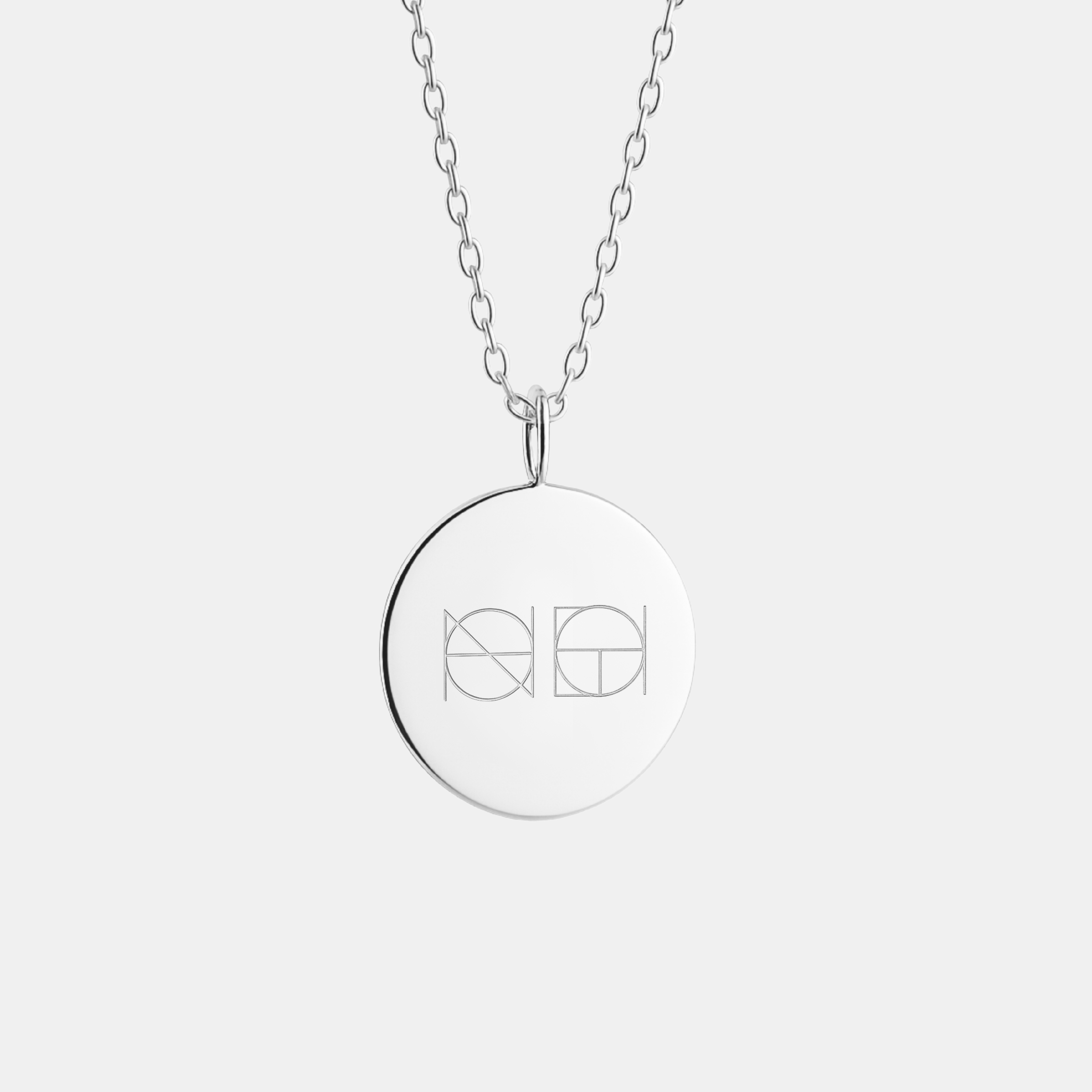 A 925 Sterling Silver coin necklace with an engraved custom Danibydsgn logo design on it, of two symbols on a light coloured background.