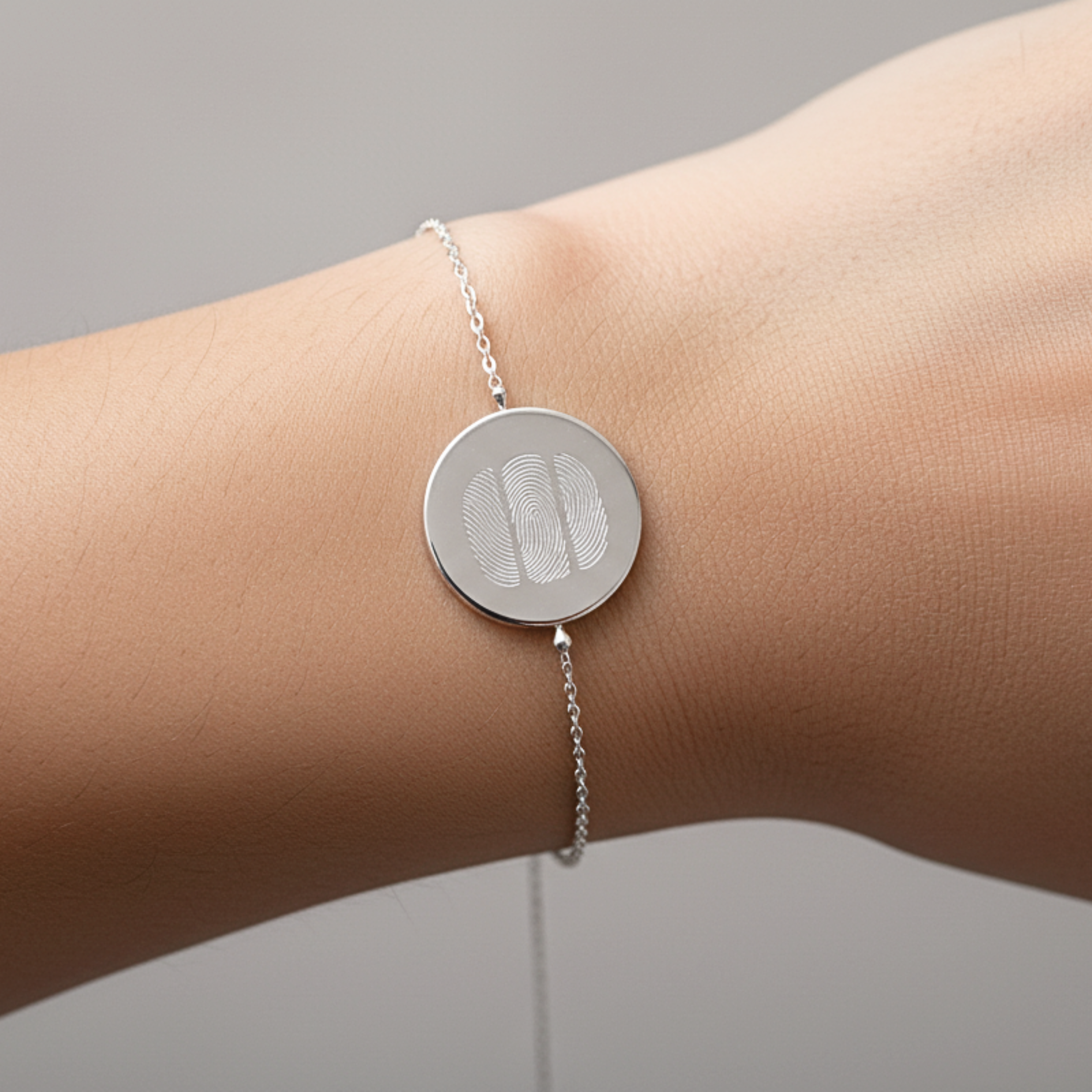 925 Sterling Silver bracelet with a circular coin pendant design engraved with three fingerprints, on a lady's wrist against a neutral background