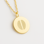 18k Gold Vermeil luxury coin pendant necklace with 2 fingerprints engraved on the pendant and pendant is on a chain on a light coloured background