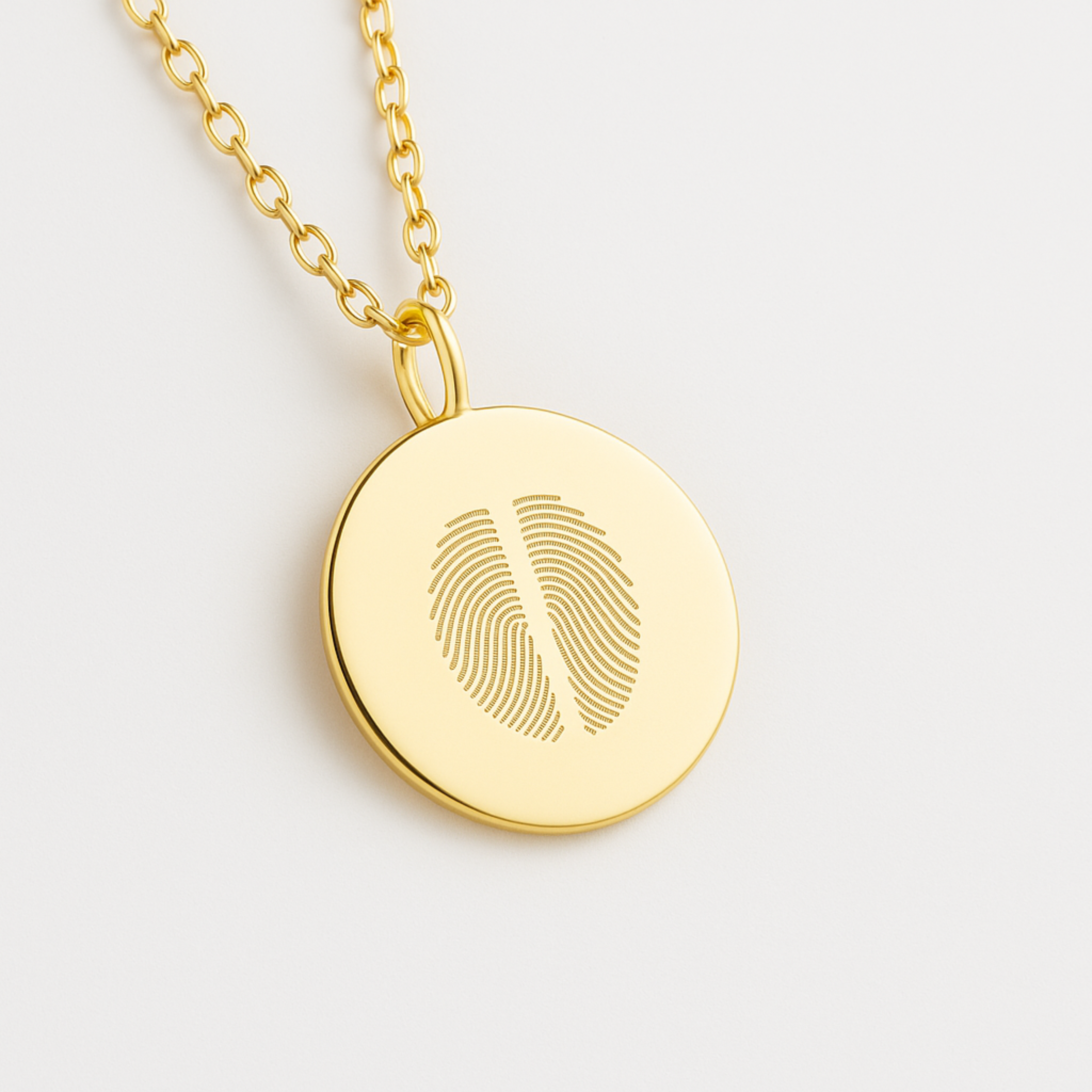 18k Gold Vermeil luxury coin pendant necklace with 2 fingerprints engraved on the pendant and pendant is on a chain on a light coloured background