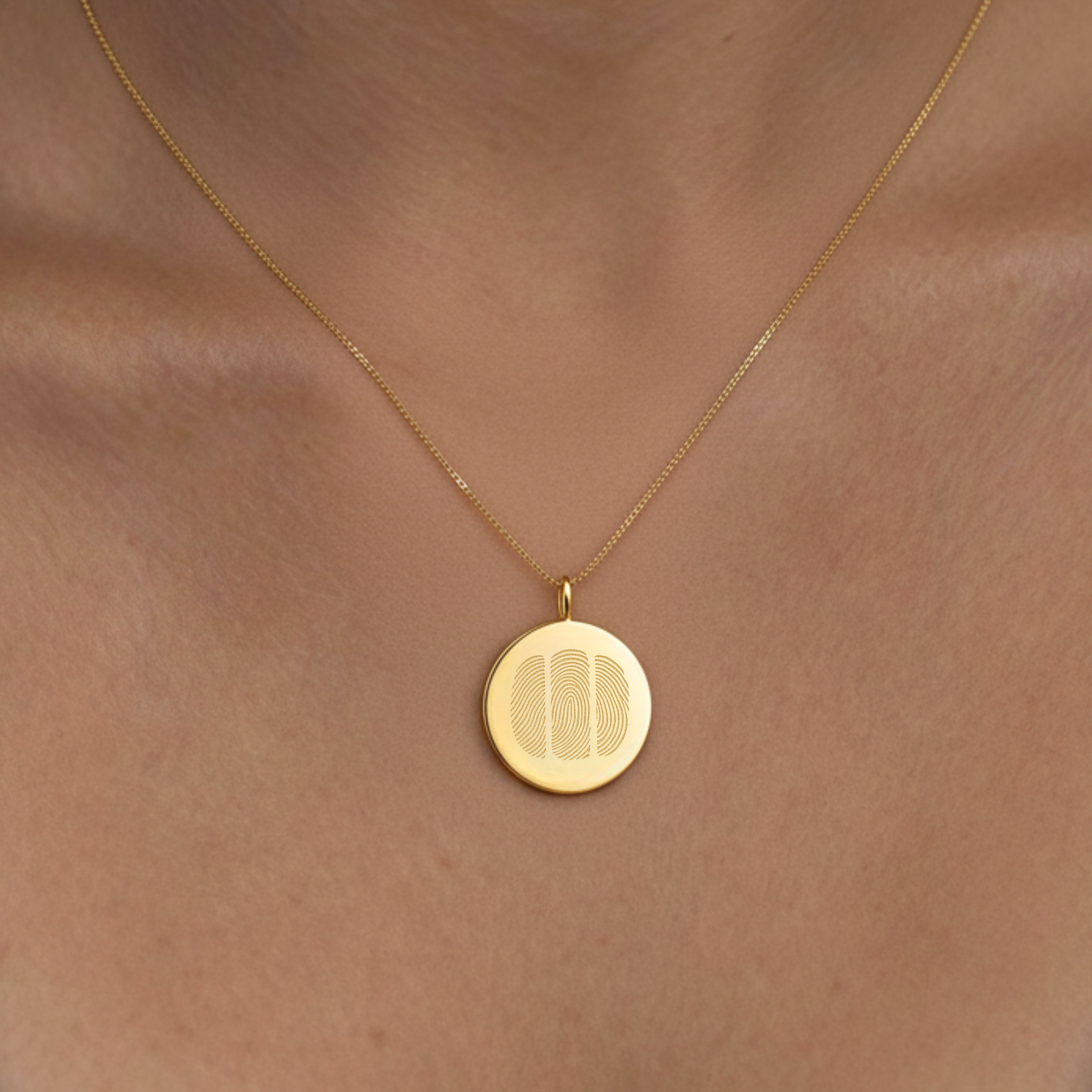 18k Gold Vermeil luxury coin pendant necklace with 3 fingerprints engraved on the pendant and pendant is on a chain and sitting around a ladies neck in a close up photo.