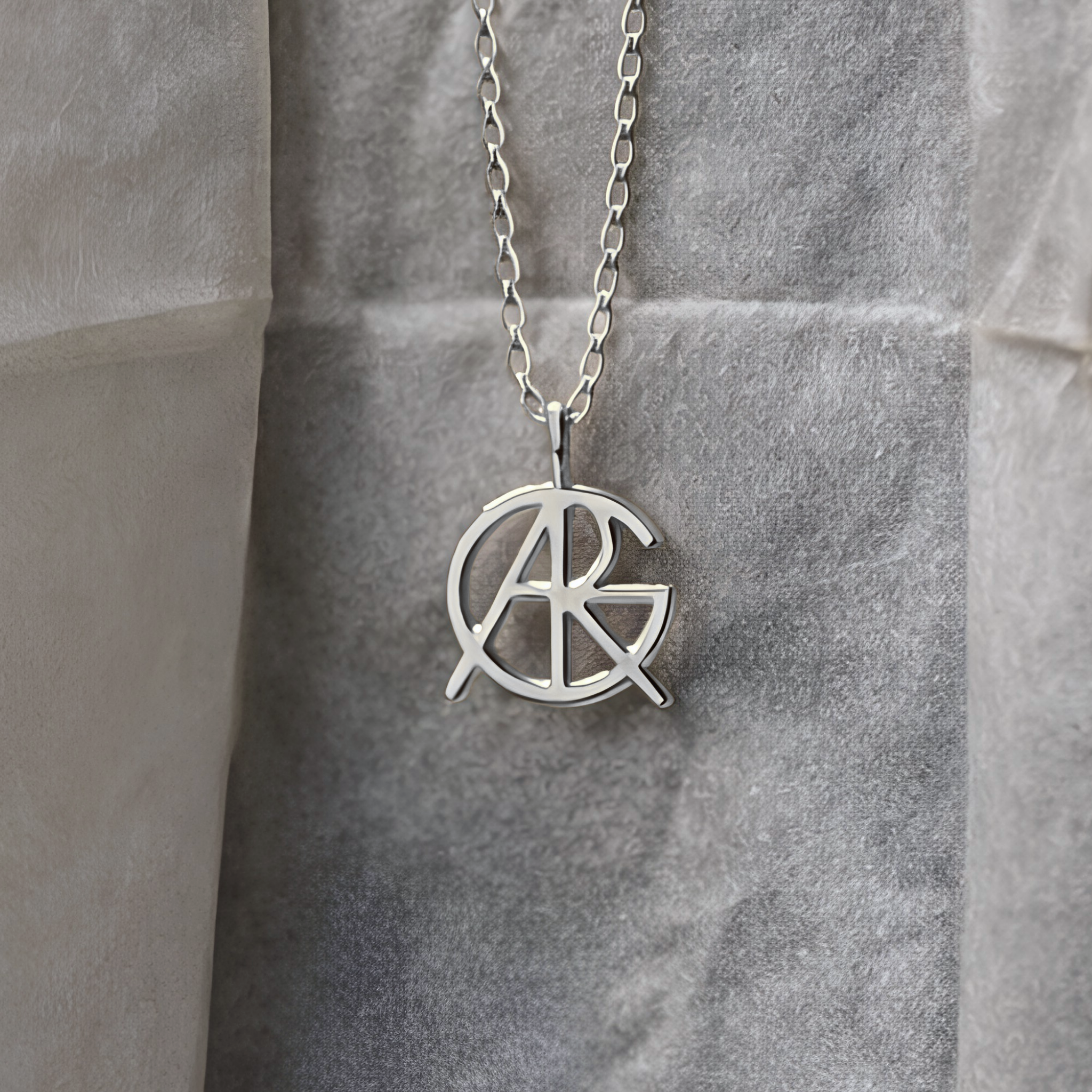 A close-up shot of a custom necklace in 925 sterling silver with a chain, highlighting a meaningful jewelry piece featuring a unique hand-designed Danibydsgn symbol cut out jewelry pendant hanging against textured paper packaging.