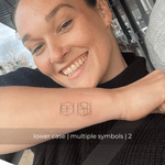 A minimalistic fine line tattoo of an overlapping Custom Logos design on a person's outer arm of a two symbol design in lowercase letters, exemplifying custom logo design, name tattoo design, and body art. This simple small tattoo idea showcases personal branding and tattoo art, ideal for both name logos and wall art applications.