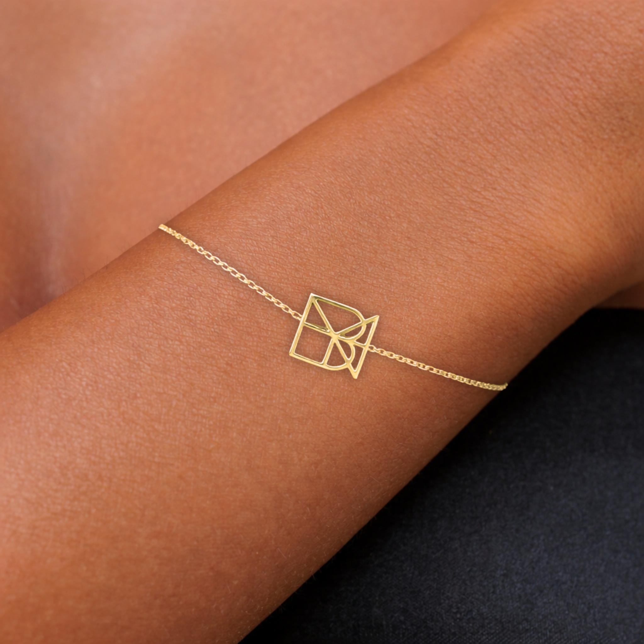 Close-up lifestyle view of a single custom 9k gold geometric symbol bracelet on a wrist, highlighting the delicate fine chain and minimalist gold design.