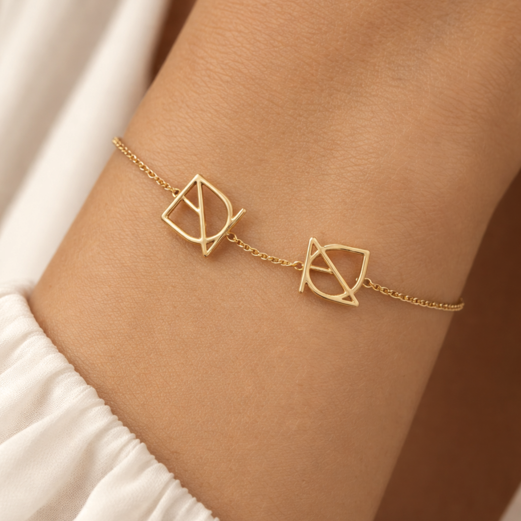 Lifestyle close-up of a custom 9k gold bracelet with two geometric symbols worn on a wrist, showcasing the warm gold finish and delicate chain.