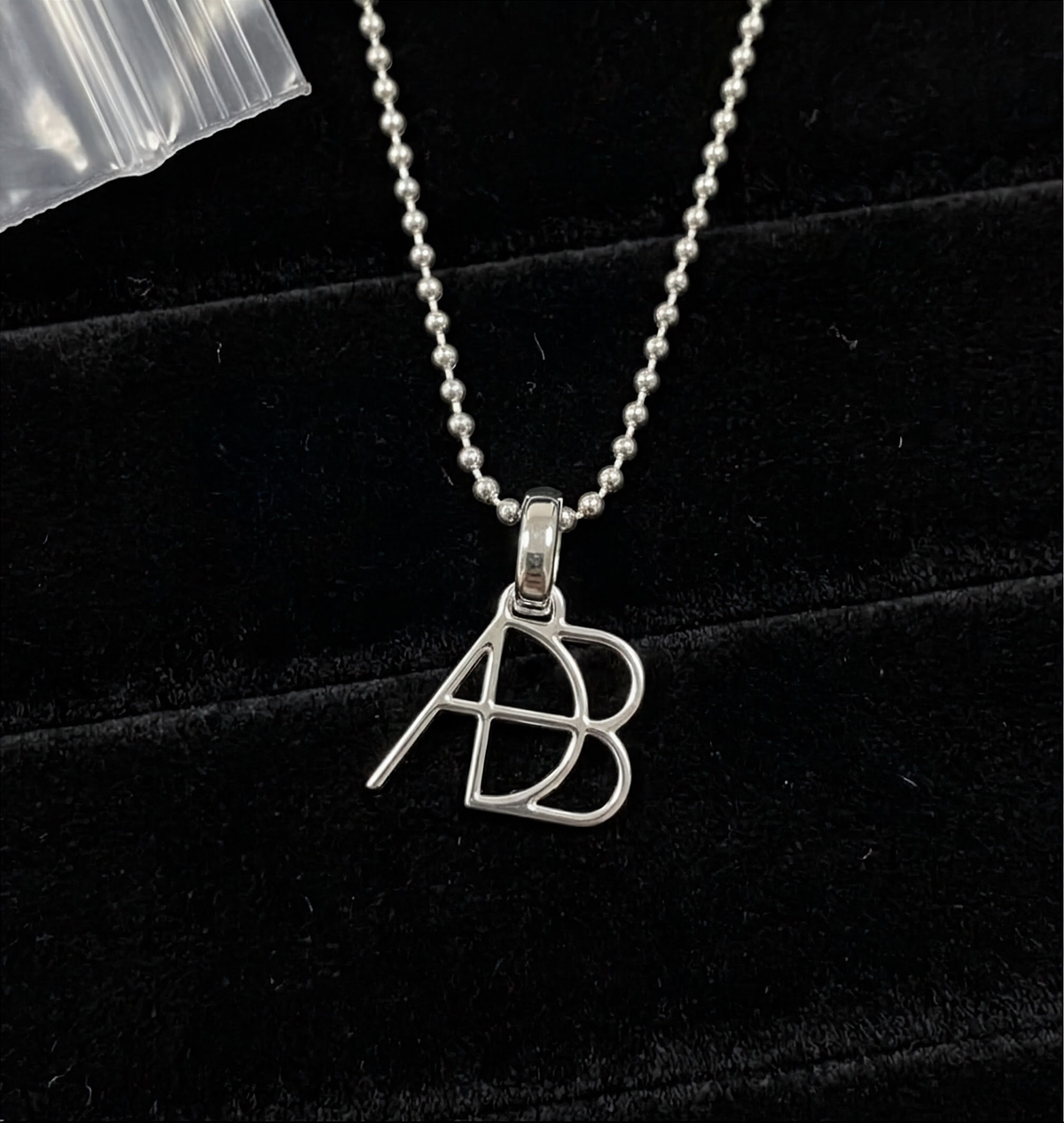 A close up of a 925 sterling silver ball chain necklace  and custom Danibydsgn symbol design clip-on charm photographed on a black velvet surface.  Meaningful personalised jewelry from Danibydsgn.