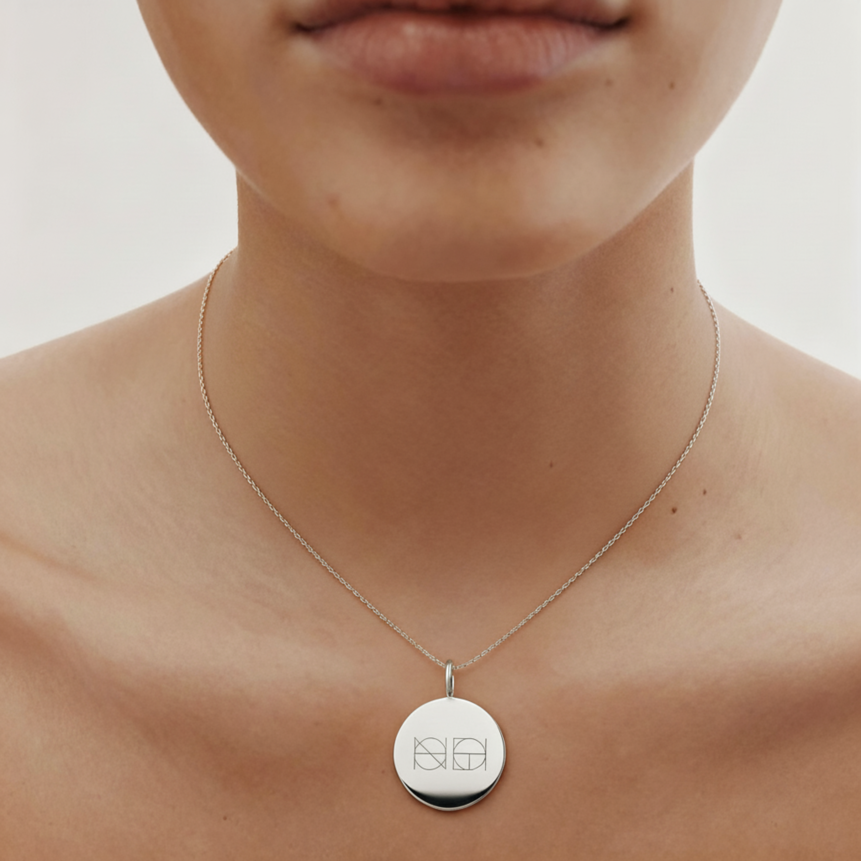 Model wearing the Danibydsgn custom engraved coin necklace in 925 sterling silver, featuring a two-symbol logo design on a polished round pendant with a fine silver chain, captured in a close-up minimal studio shot.