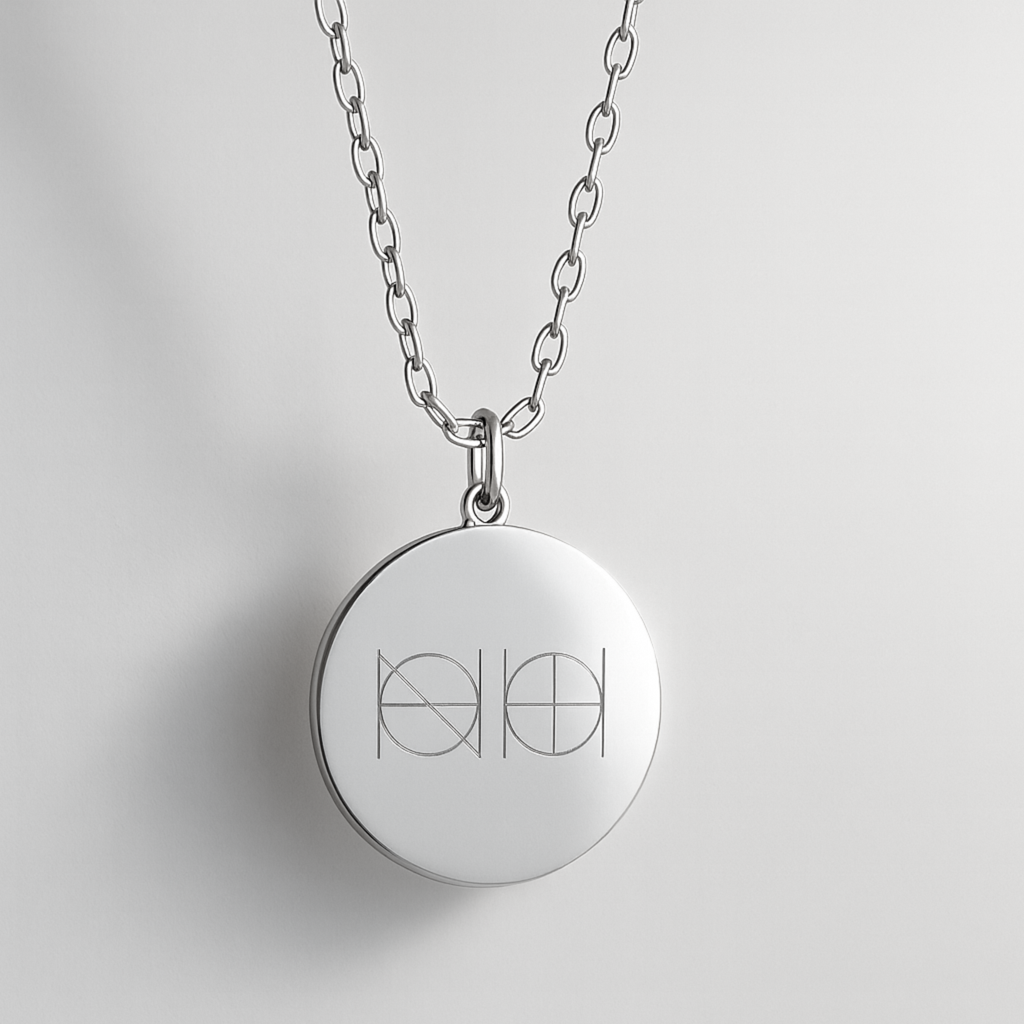 Close-up view of the Danibydsgn custom engraved coin necklace in 925 sterling silver, featuring a sleek two-symbol logo engraving on a polished round pendant suspended from a fine silver chain against a soft light background.