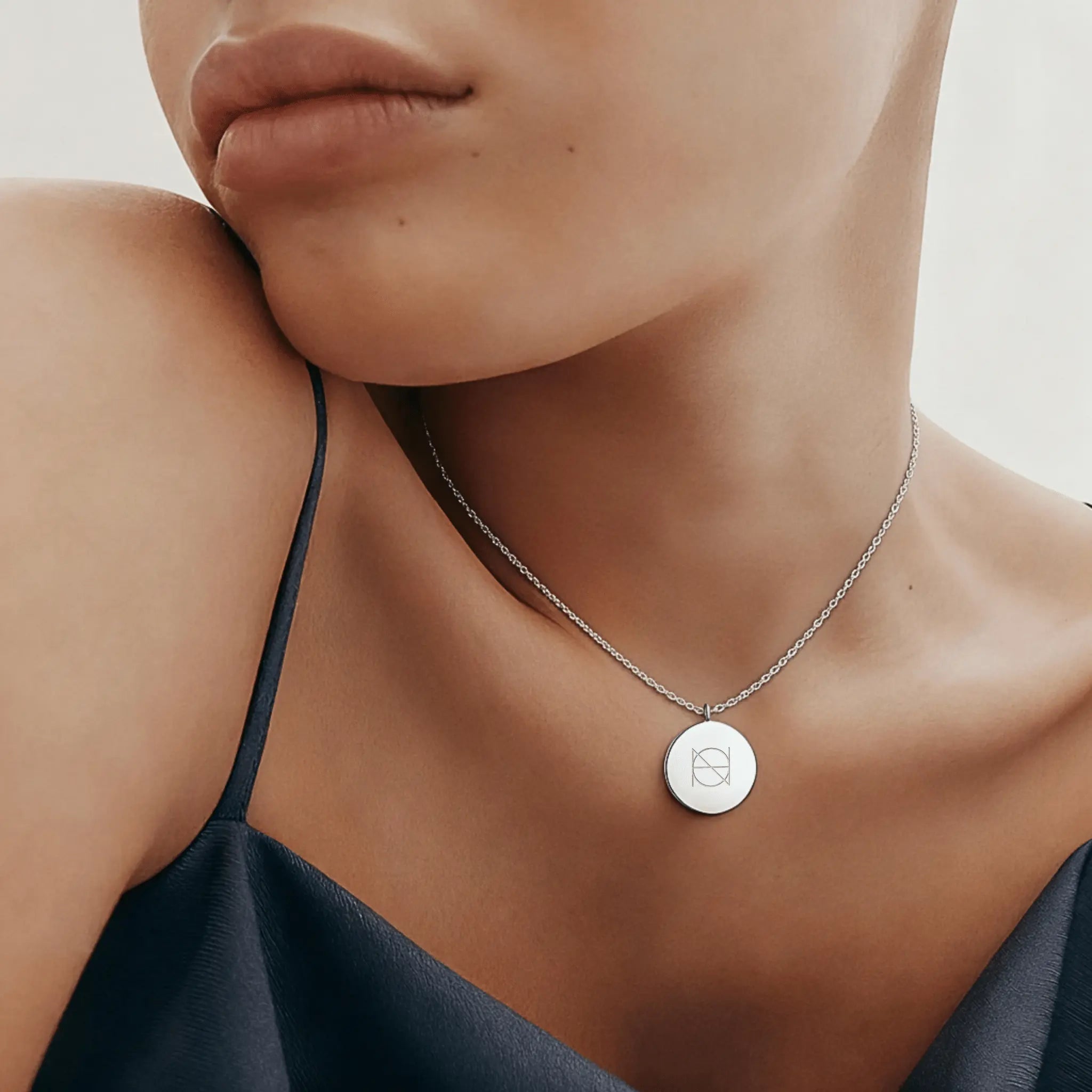 Custom engraved coin necklace in 925 sterling silver worn by a model in a camisole, showcasing luxury jewelry design.