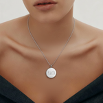 Danibydsgn custom engraved coin necklace in 925 sterling silver, shown on a model wearing a dark off-shoulder outfit. The polished pendant features the brand’s minimal two-symbol logo engraving for an elegant and timeless look.