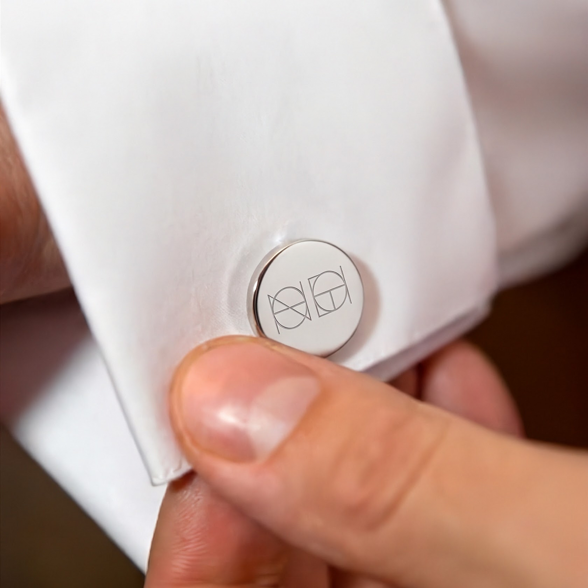 A close-up of a white dress shirt cuff with a round 925 sterling silver cufflink featuring a custom engraving of a Danibydsgn custom symbol.