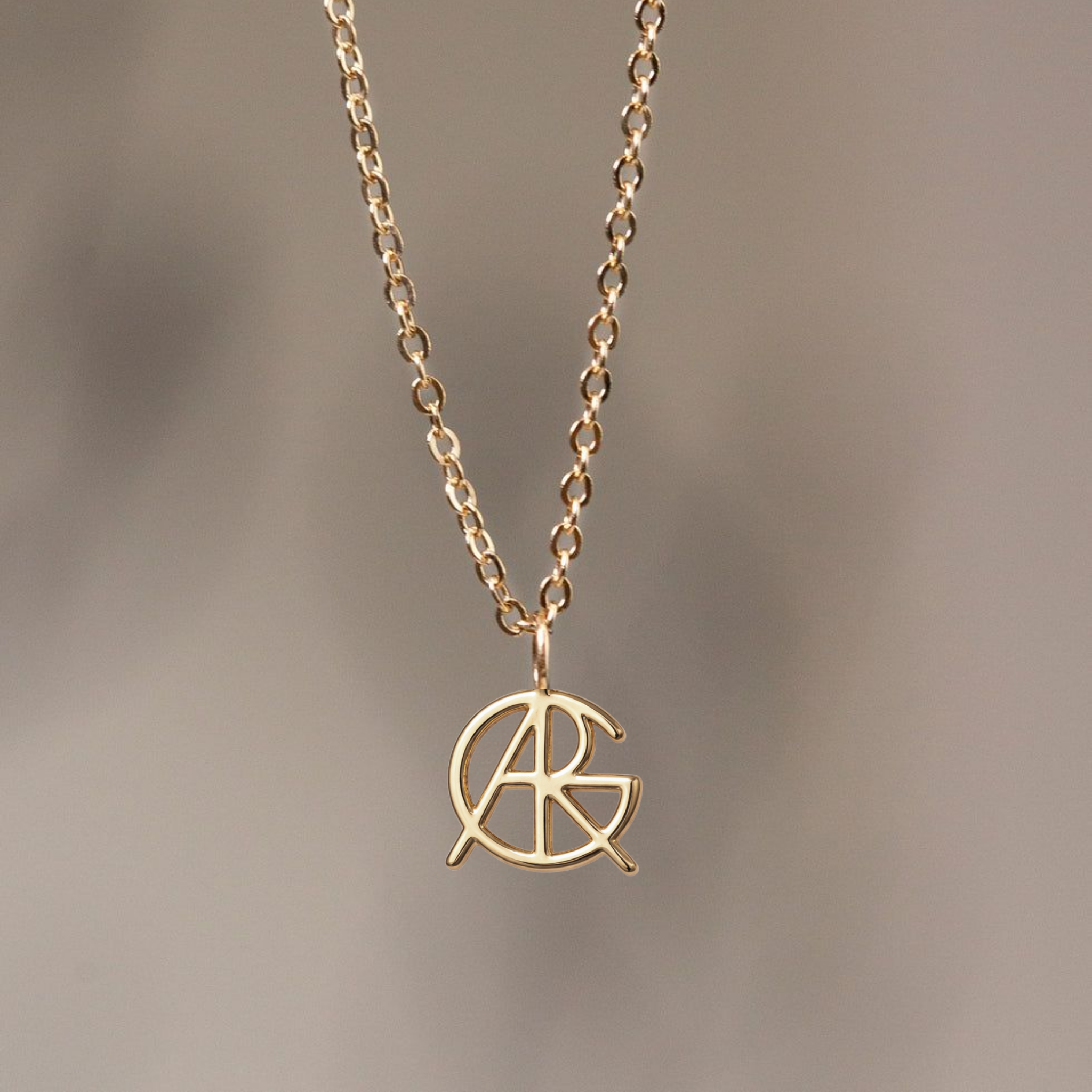 A close-up shot of a custom necklace in 9k gold with a chain, highlighting a meaningful jewelry piece featuring a unique hand-designed Danibydsgn symbol cut out jewelry pendant hanging against a soft neutral background.