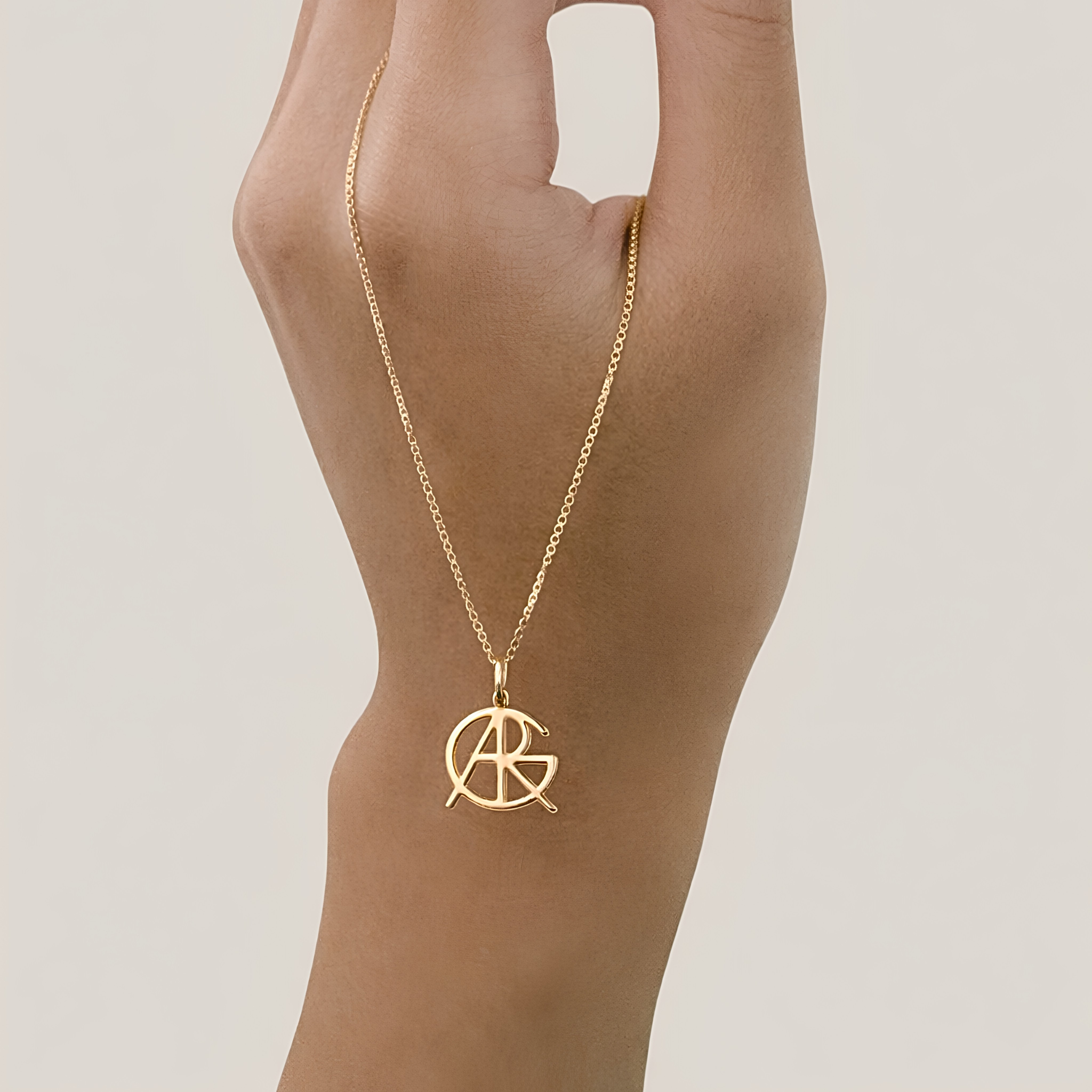 A hand holding up a custom necklace in 9k gold, showcasing a piece of meaningful jewelry with a unique hand-designed Danibydsgn symbol cut out jewelry pendant hanging from a central jump ring.