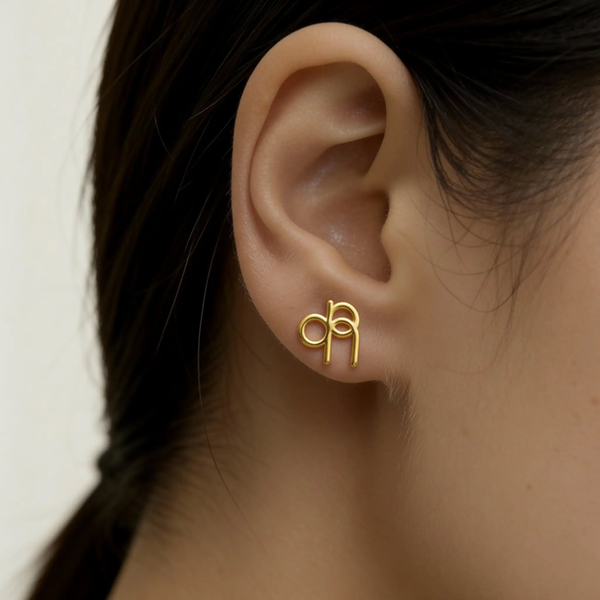 Danibydsgn custom symbol stud earring in 9k Gold worn on a lady's ear, featuring a cut-out exact silhouette of a Danibydsgn design.