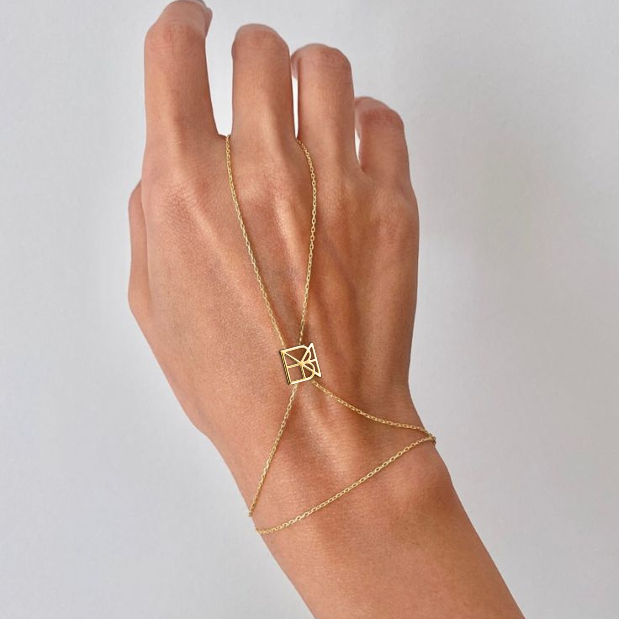 Danibydsgn custom symbol hand chain in 9K gold worn on hand against a light grey background, featuring a geometric cut-out symbol connector.