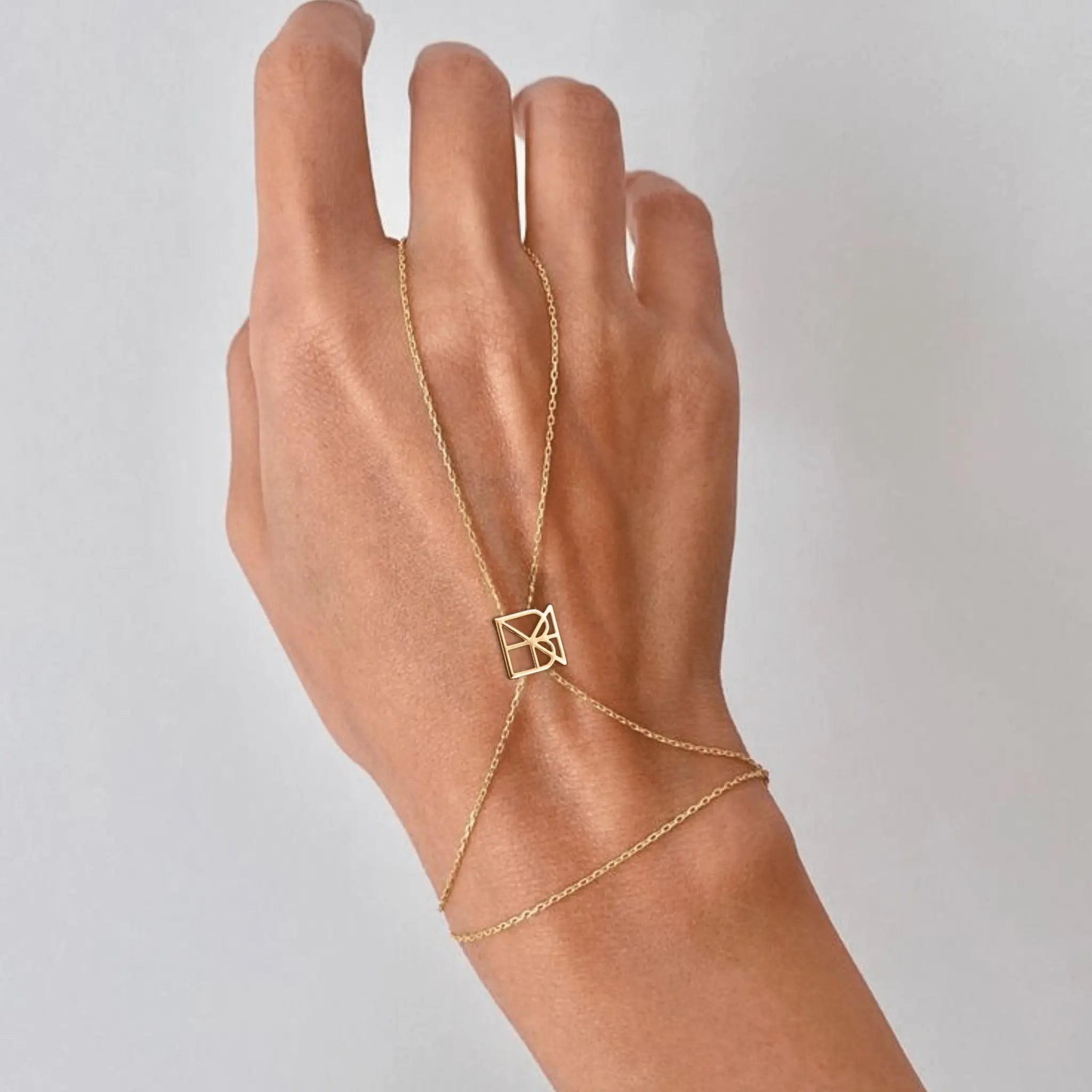 Danibydsgn custom symbol hand chain in 9K gold worn on hand against a light grey background, featuring a geometric cut-out symbol connector.