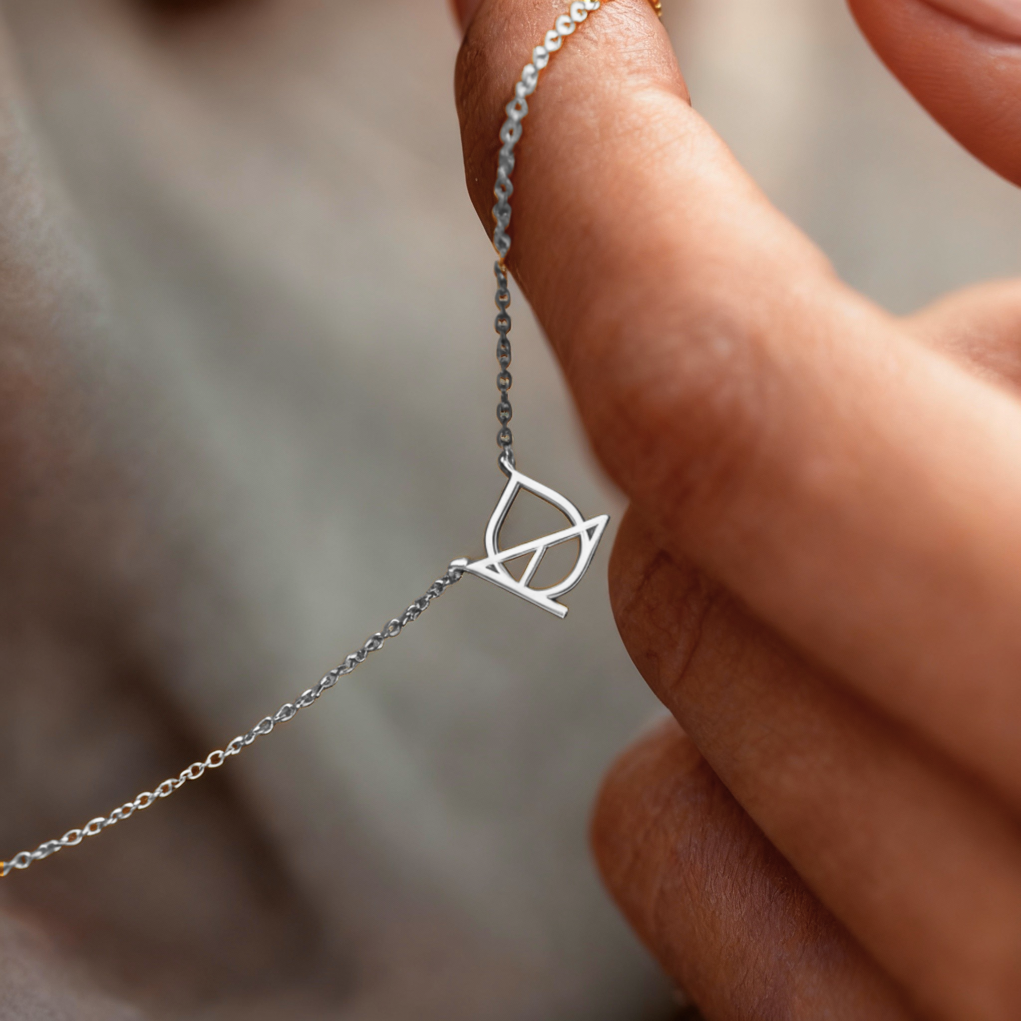 Close-up of Danibydsgn custom symbol necklace in 925 sterling silver, showing the cut-out silhouette pendant held between fingers on a fine chain.