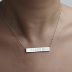 Close-up of the Danibydsgn engraved bar necklace in 925 sterling silver, shown worn on a model’s neck. The polished rectangular pendant features a four-symbol geometric engraving and hangs from a delicate silver chain.