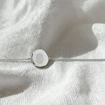 Elegant flatlay of the Danibydsgn Single Fingerprint Coin Bracelet in 925 Sterling Silver, displayed on softly textured white fabric, featuring a delicately engraved fingerprint on a polished circular pendant with a fine chain.