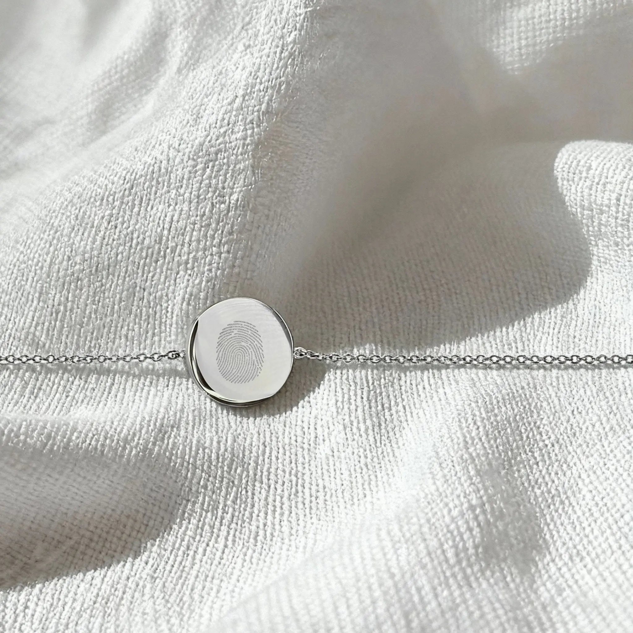 Single fingerprint coin bracelet in 925 sterling silver by Danibydsgn, displayed in a flatlay arrangement.